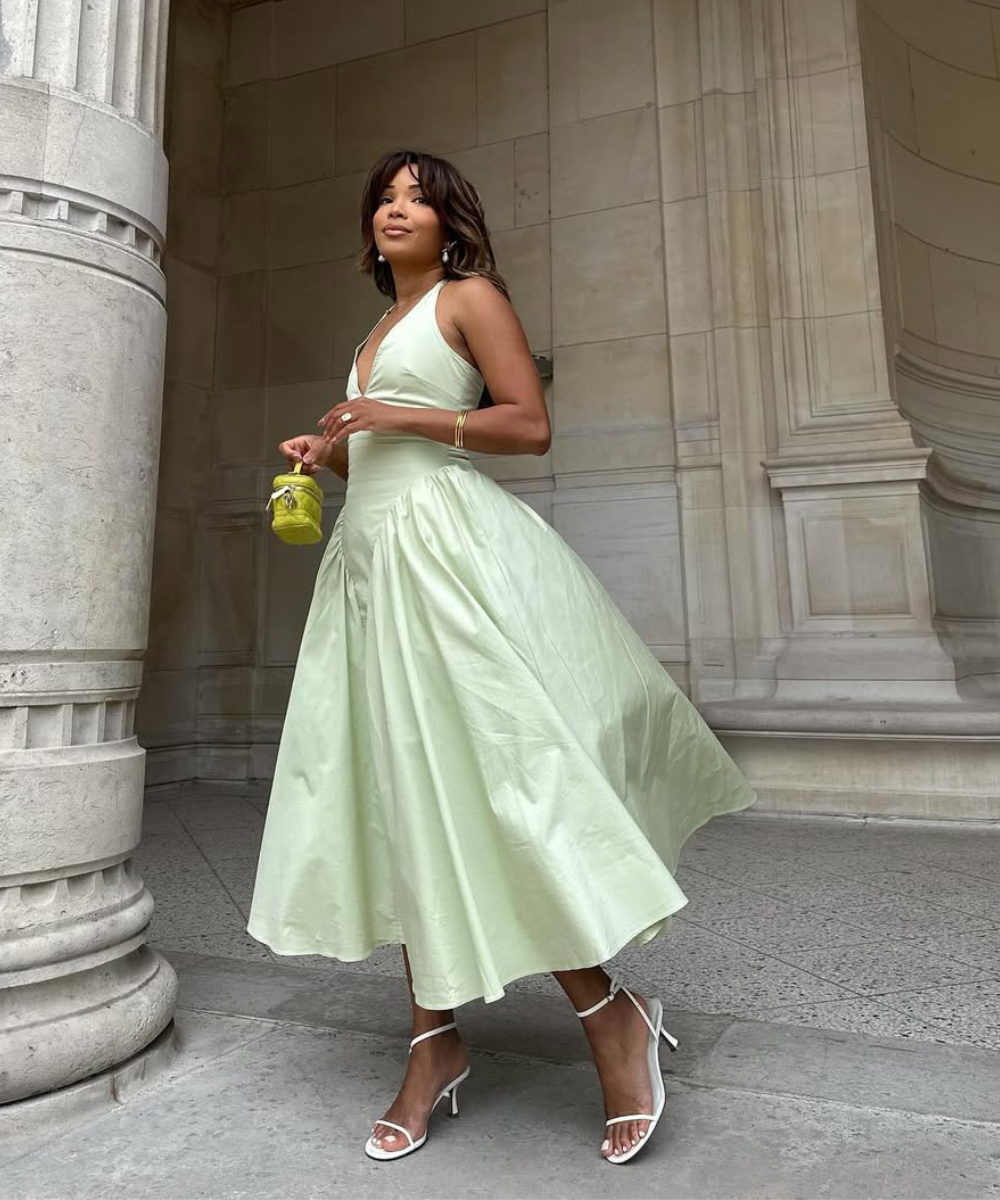Mulher usando vestido verde claro e sandália branca feminina, segurando bolsa pequena amarela.