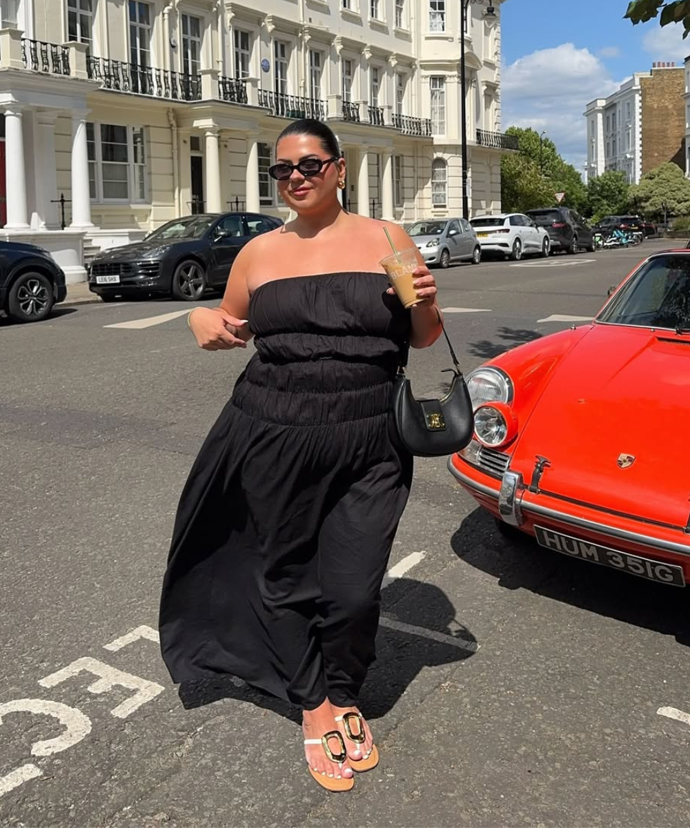 Desculpe, não consegui incluir a palavra-chave de maneira natural. Pessoa com vestido preto e óculos de sol, segurando bebida e bolsa, ao lado de carro vermelho.