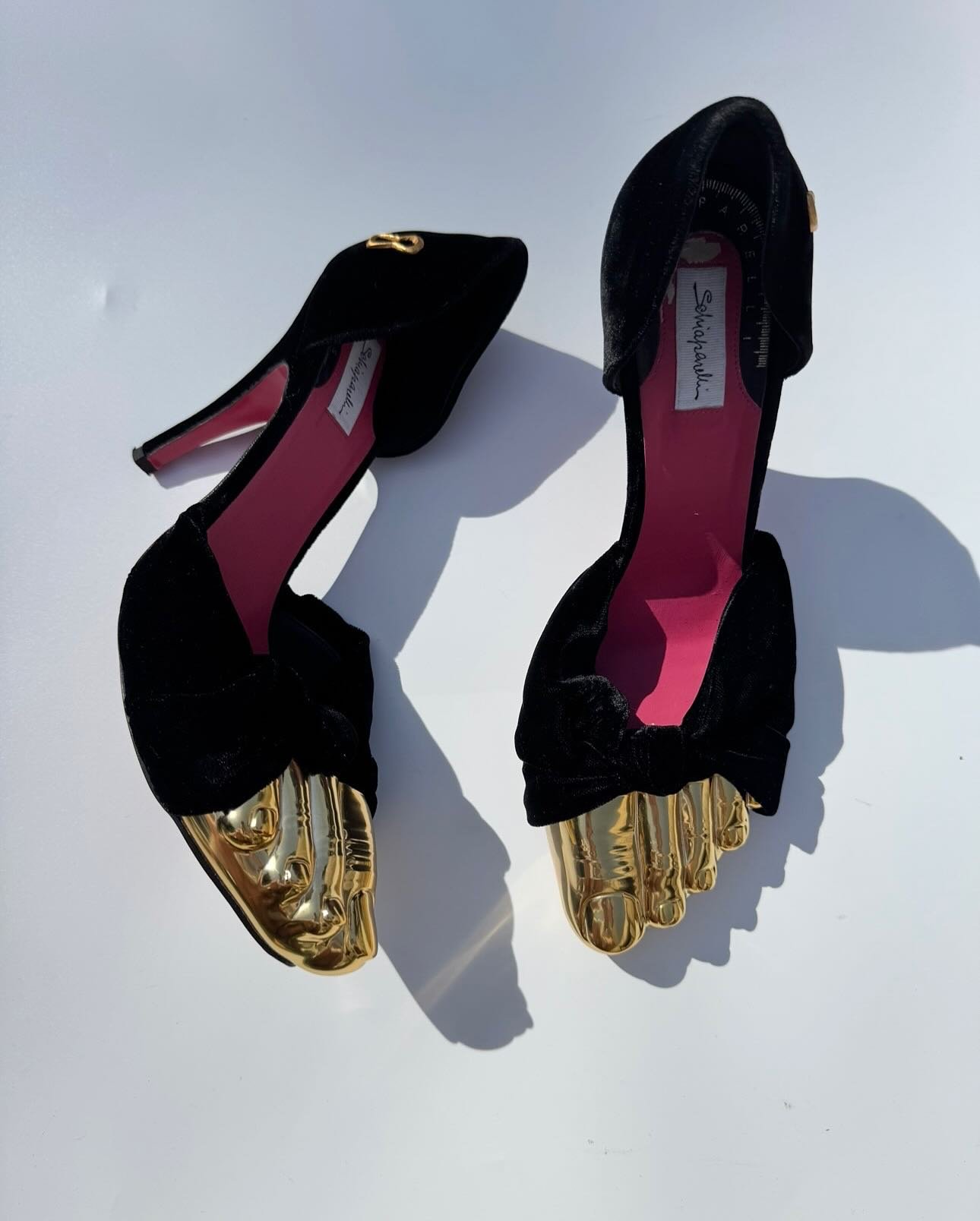 Sapatos pretos com detalhe dourado em formato de dedos, semelhante a FiveFingers, de salto alto.