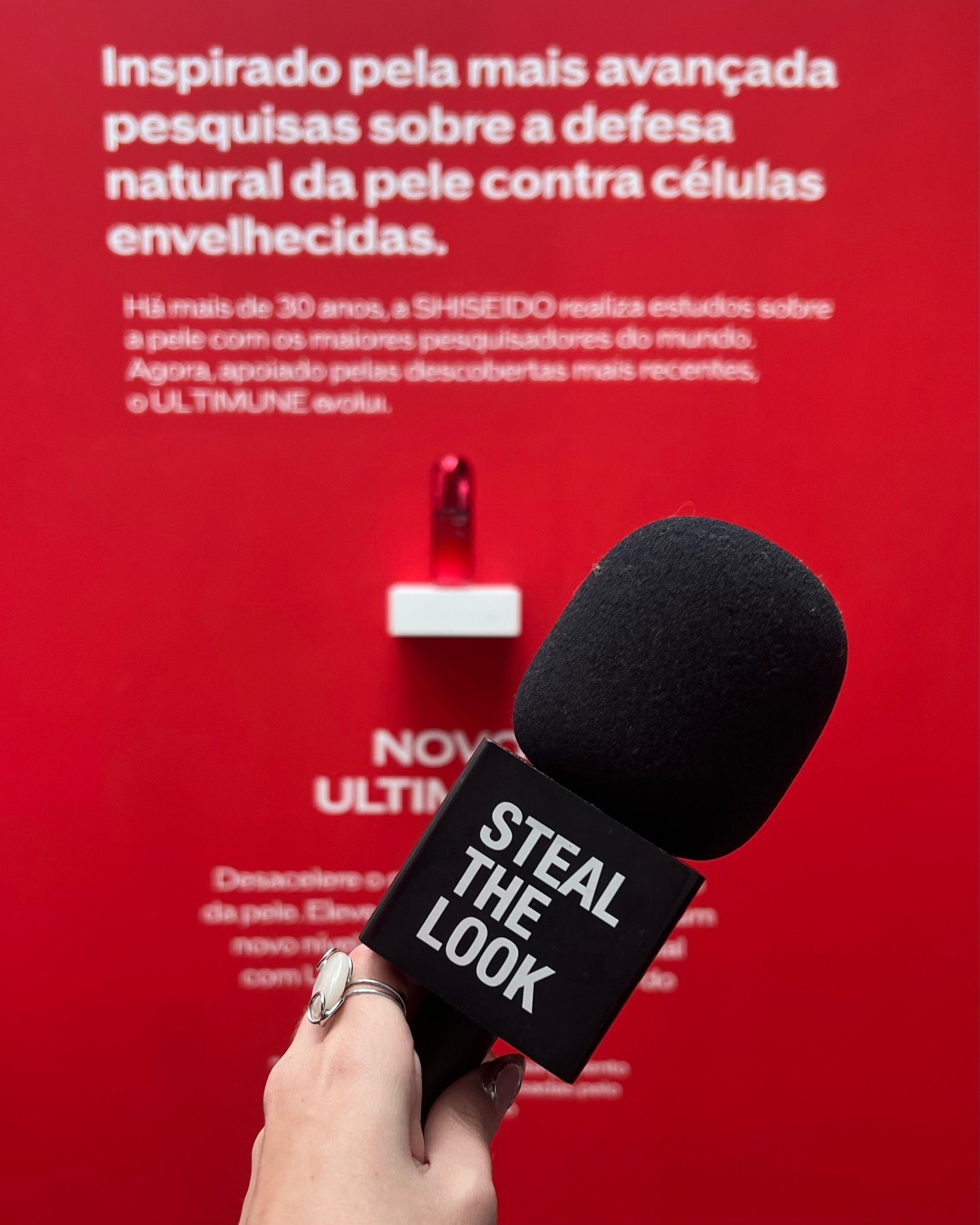 Fundo vermelho com texto sobre pesquisas de defesa da pele pela Shiseido. Microfone com 