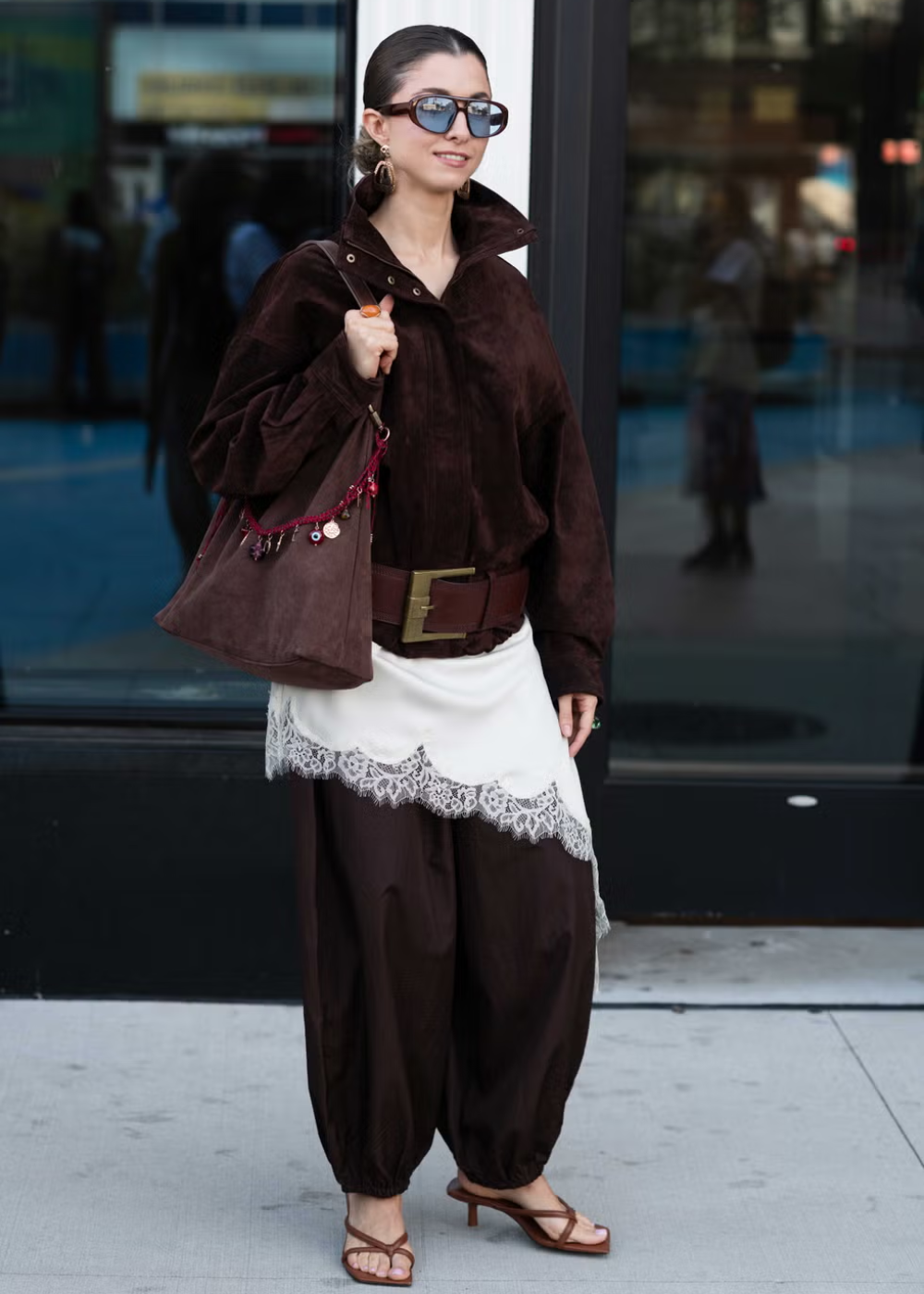 Mulher com traje marrom de veludo, saia branca com renda e bolsa no street style da NYFW.
