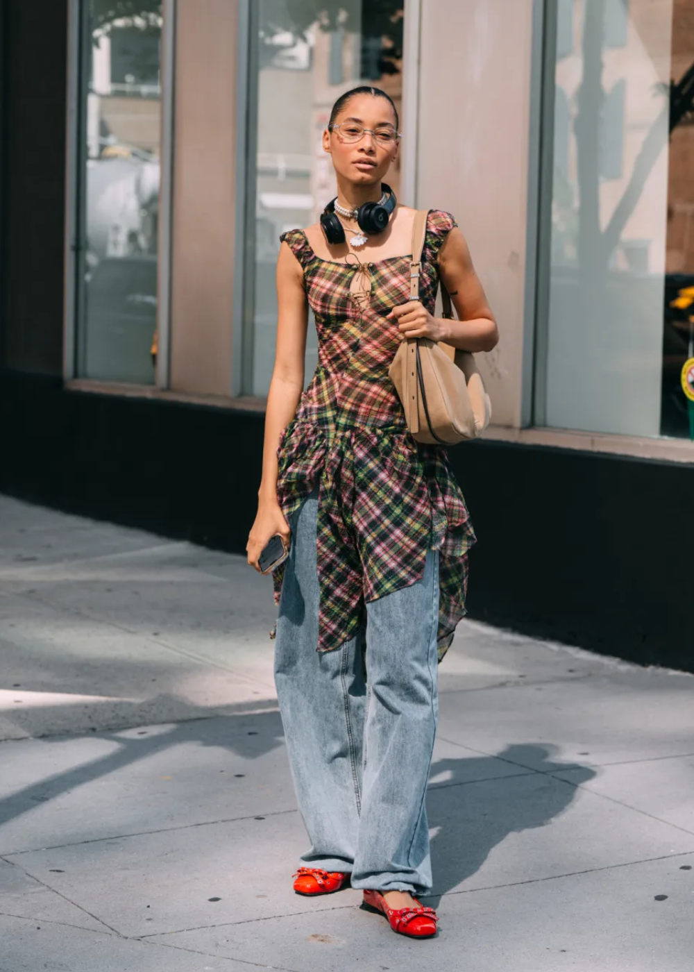 Pessoa com blusa xadrez, jeans largos e sapatos vermelhos, destacando-se nos looks do street style da NYFW.