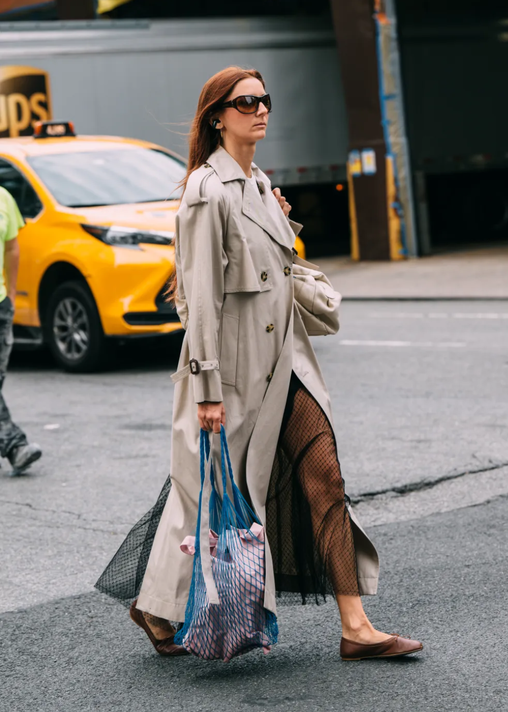 Mulher com trench coat bege sobre vestido preto transparente caminha em Nova York, simbolizando looks do street style da NYFW.