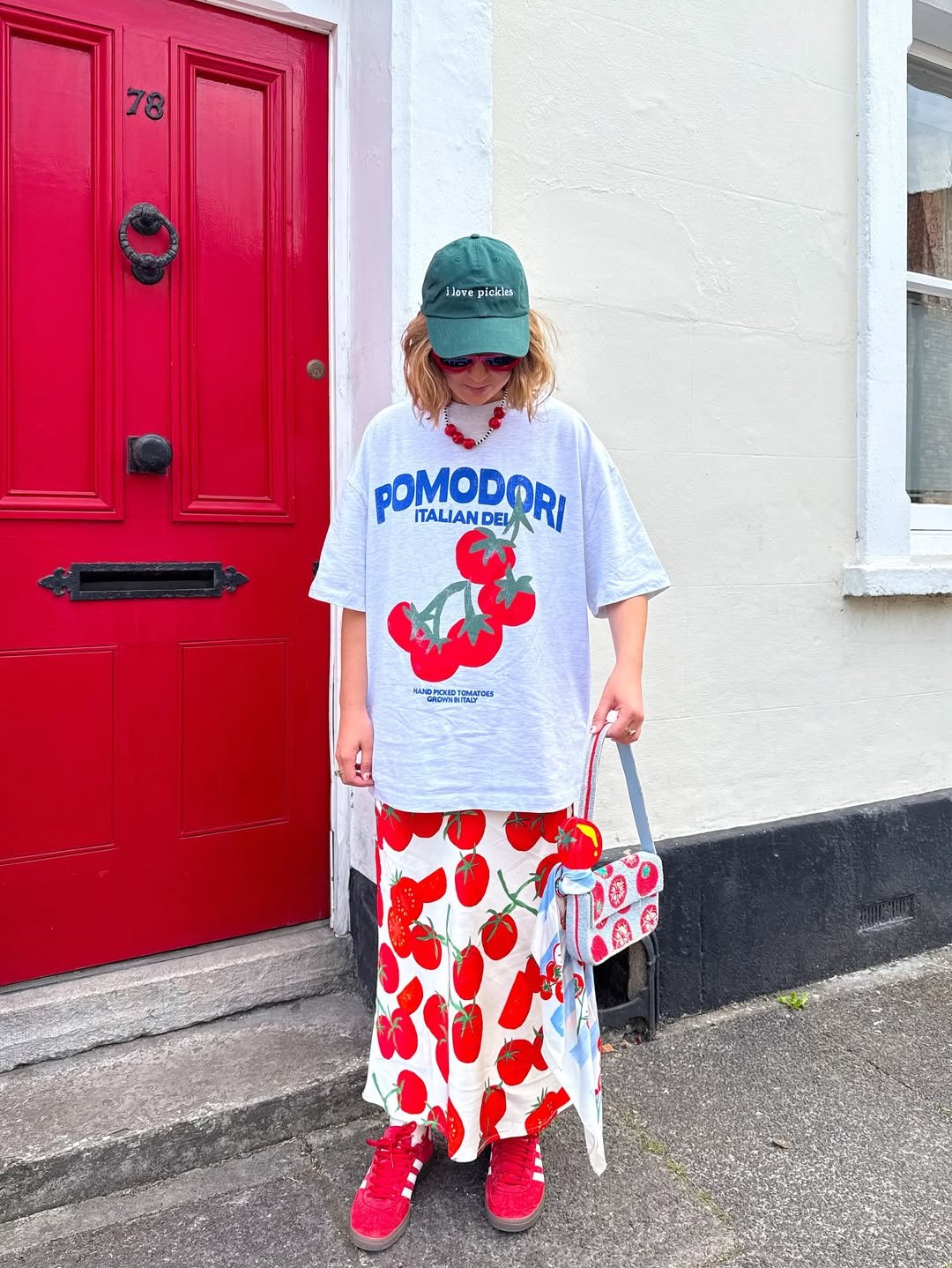Pessoa vestindo camiseta e saia com estampas de vermelho tomate em frente a uma porta vermelha.