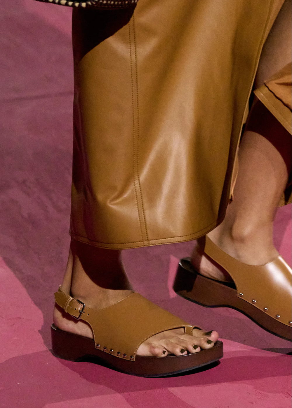 Sandálias de couro marrom com salto de madeira em desfile, combinadas com saia longa.