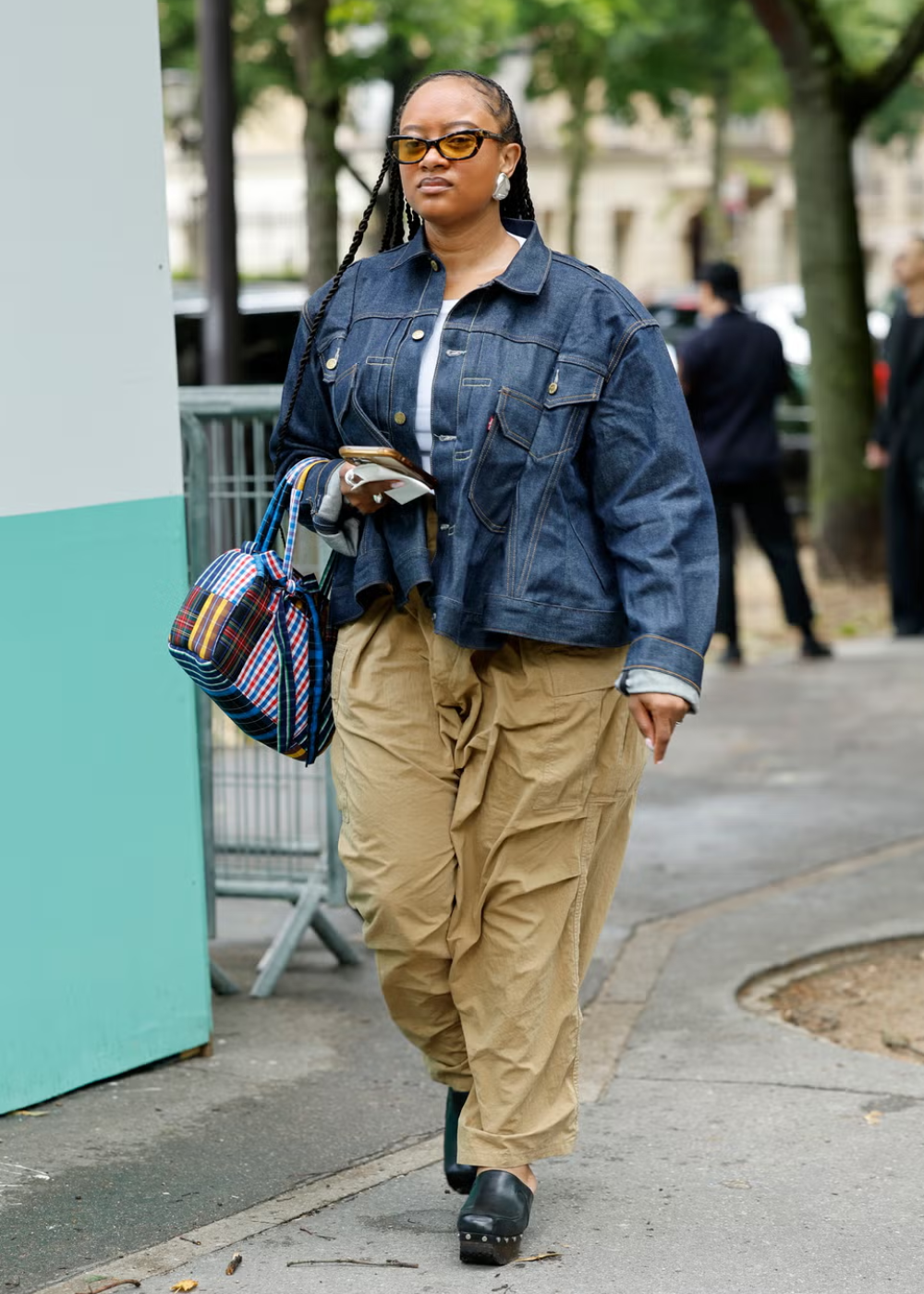 Pessoa caminhando em um parque, vestindo jaqueta jeans e calças bege, usando tamanco de madeira.