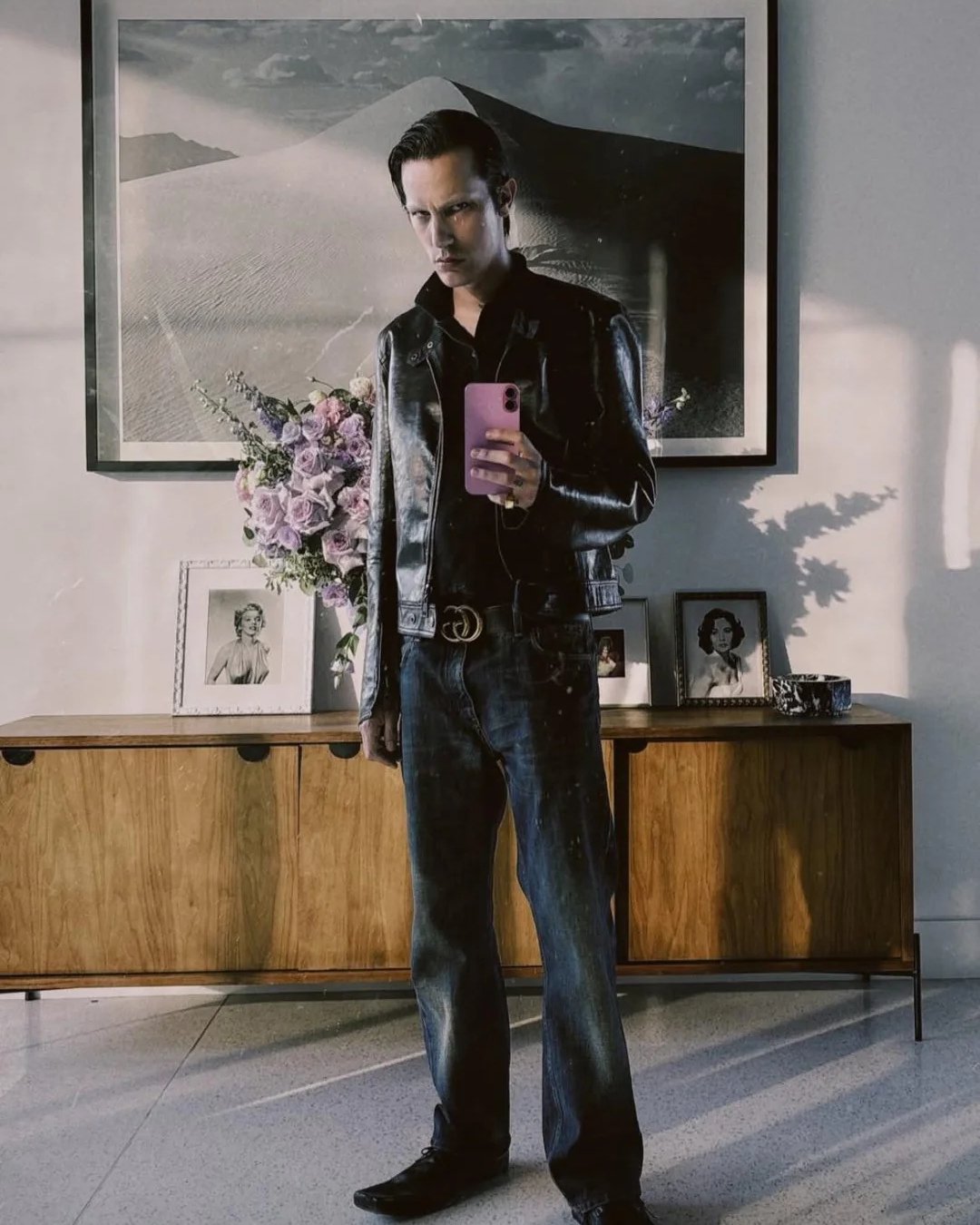 Pessoa em look de couro e jeans, refletindo estilo ousado para a temporada de moda em frente a aparador e quadros.