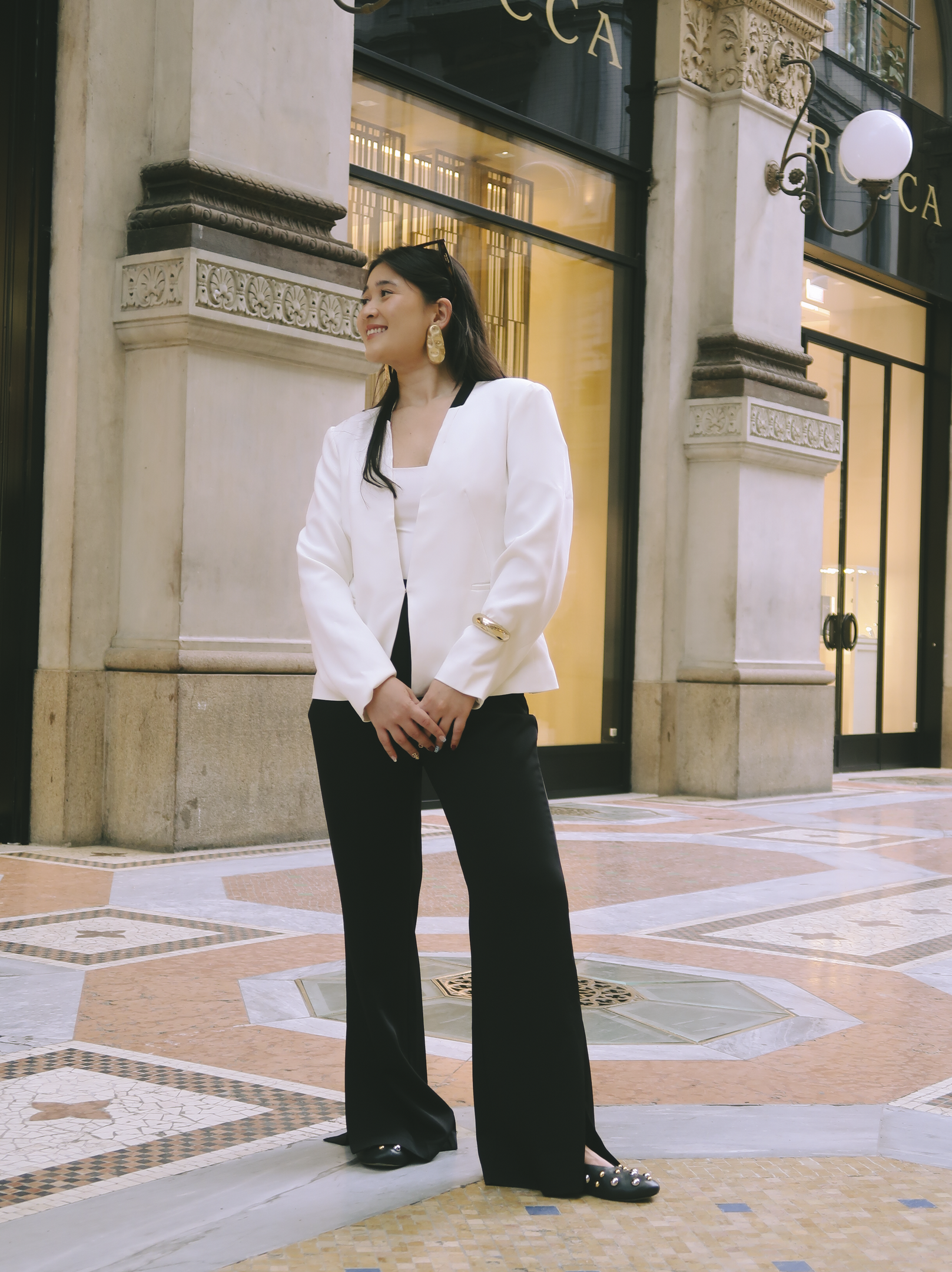 Mulher com blazer branco e calça preta usa flats elegantes. Cenário urbano sofisticado.