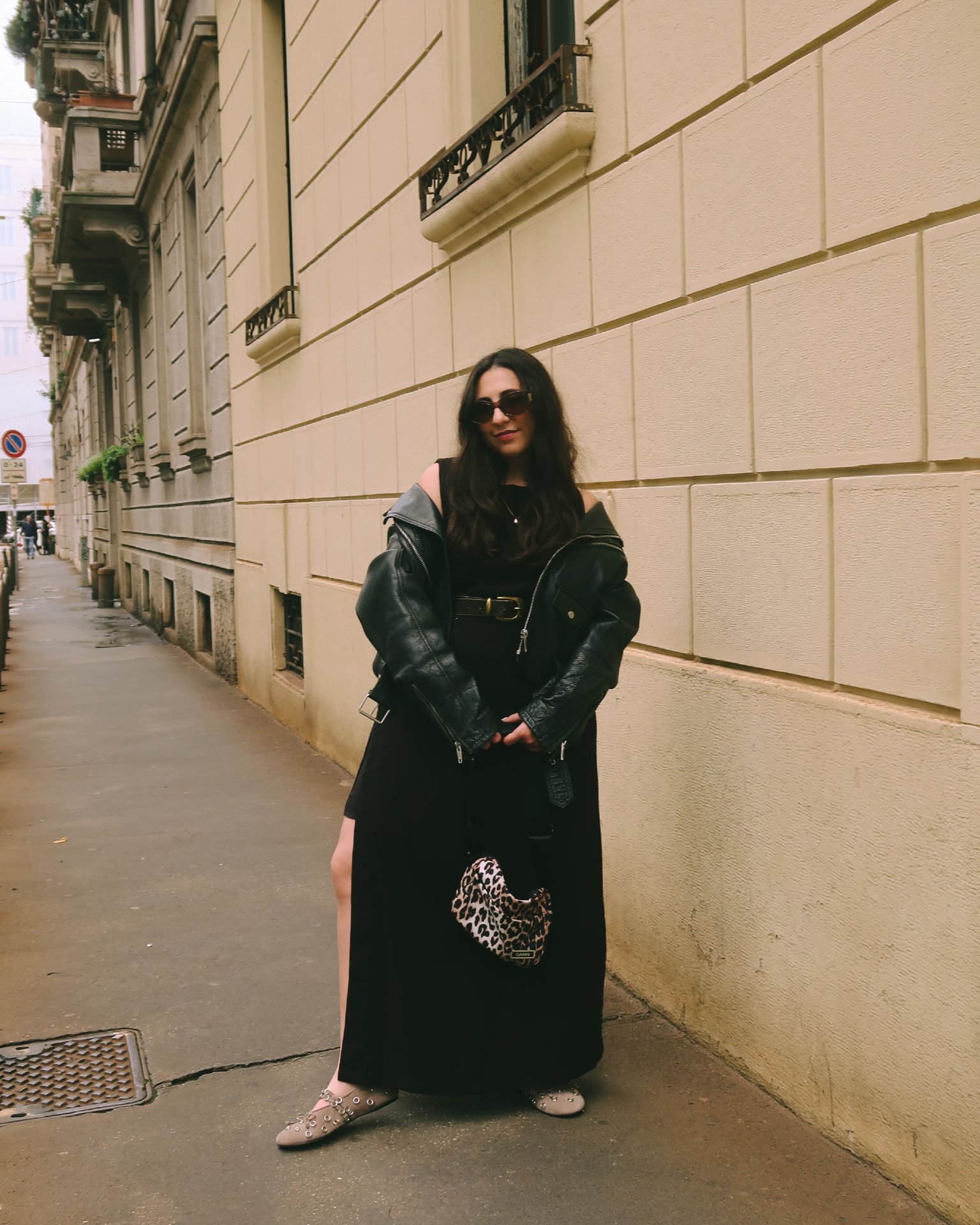 Pessoa em vestido preto e jaqueta de couro, usando flats decoradas, em rua urbana.