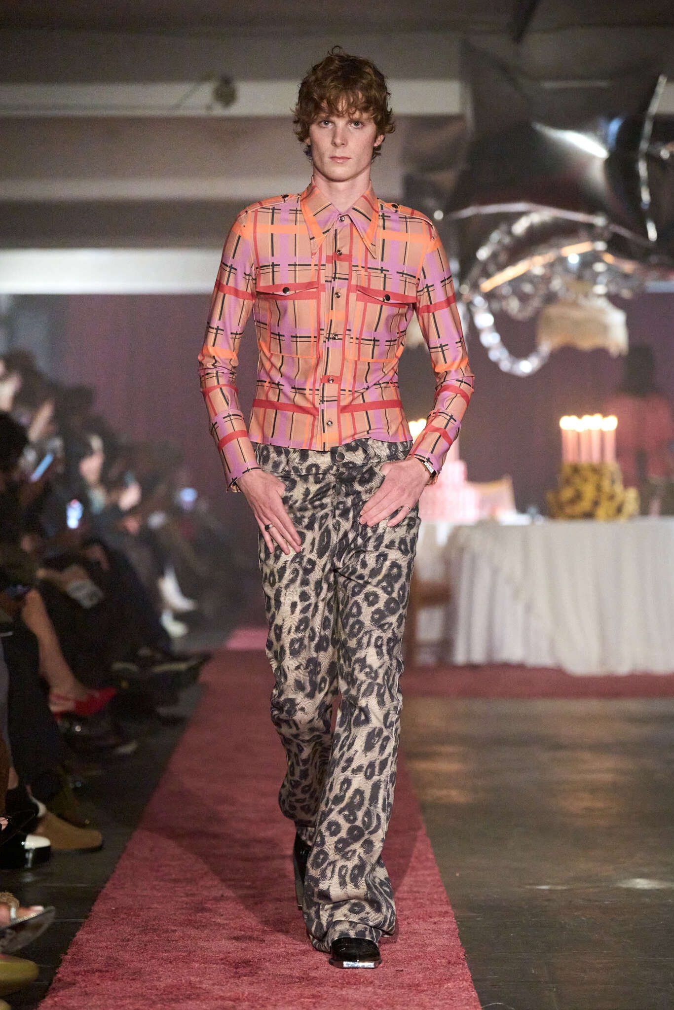 Modelo desfila com camisa xadrez rosa e calça de estampa animal. Evento: London Fashion Week SS26.