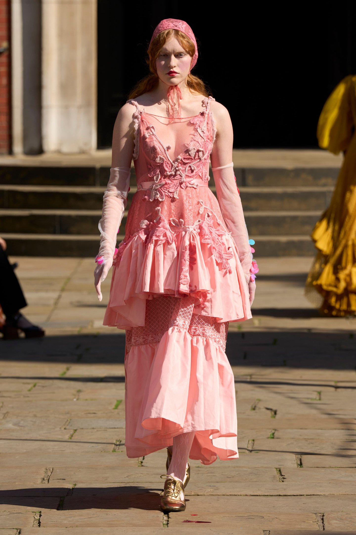 Modelo desfilando em vestidão rosa com babados e bordados na London Fashion Week SS26.