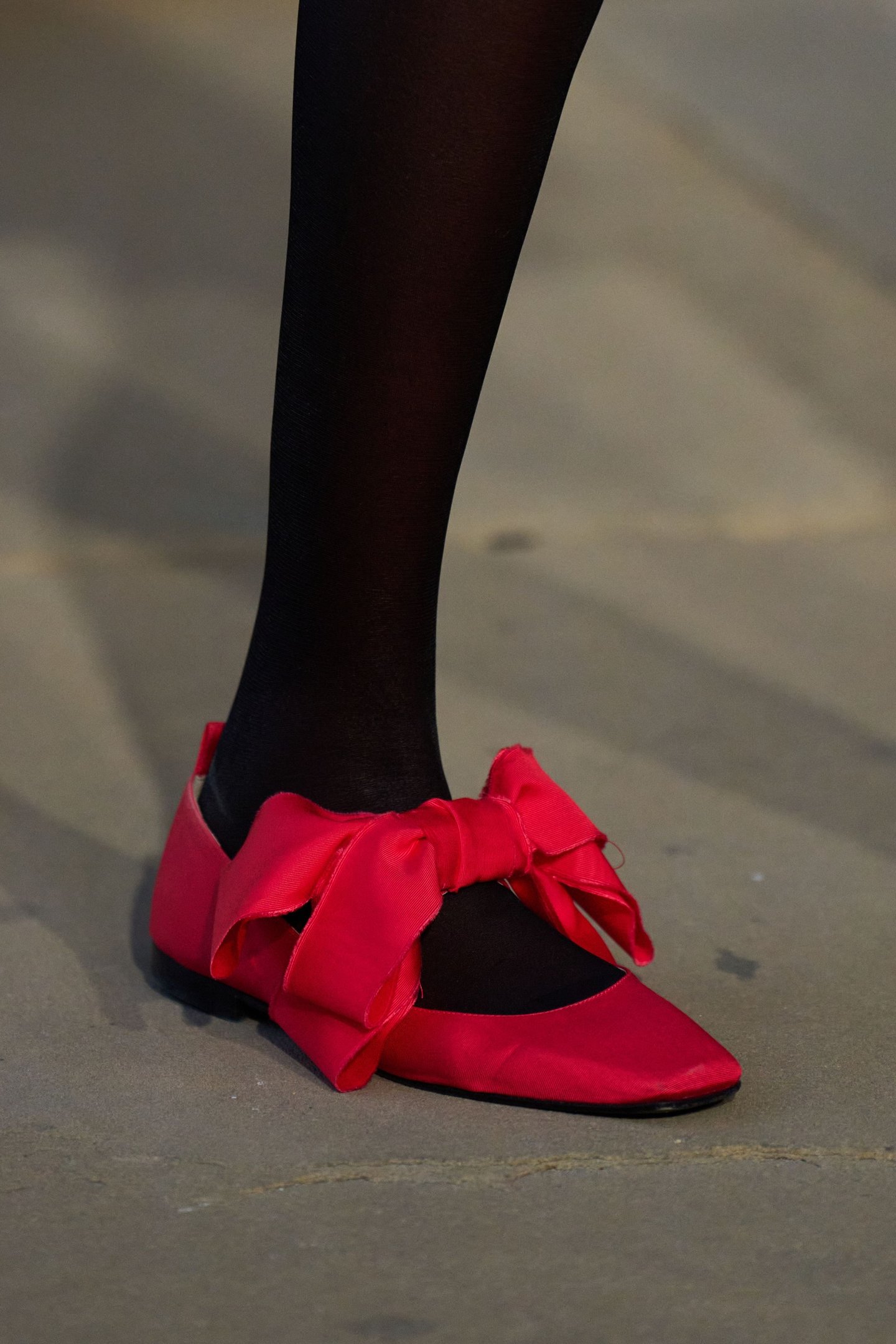 Sapatilha vermelha com laço grande sobre meia preta, destacada na London Fashion Week SS26.