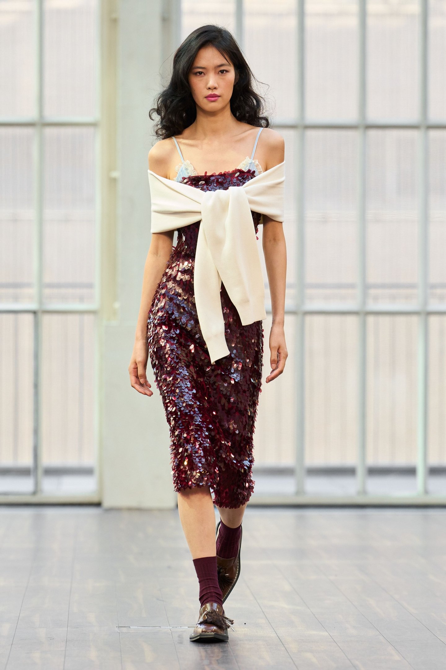 Modelo usando vestido de lantejoulas vinho e suéter creme. Desfile London Fashion Week SS26.