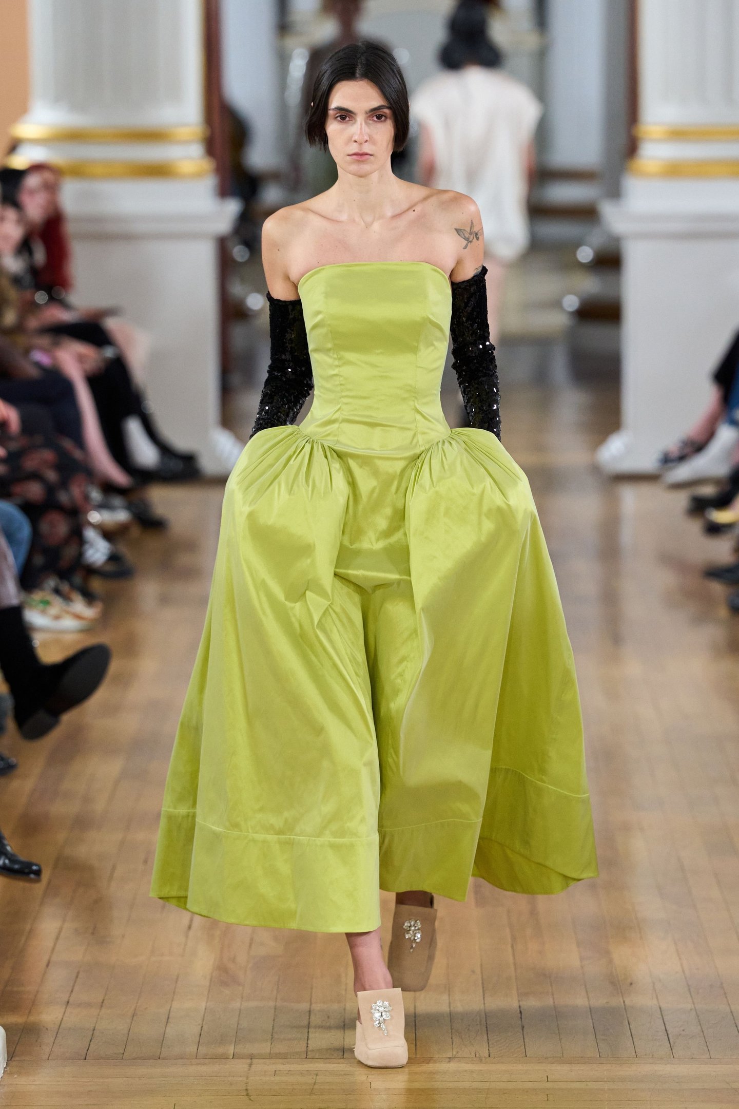 Modelo desfila em vestido verde vibrante com braços cobertos, na London Fashion Week SS26.