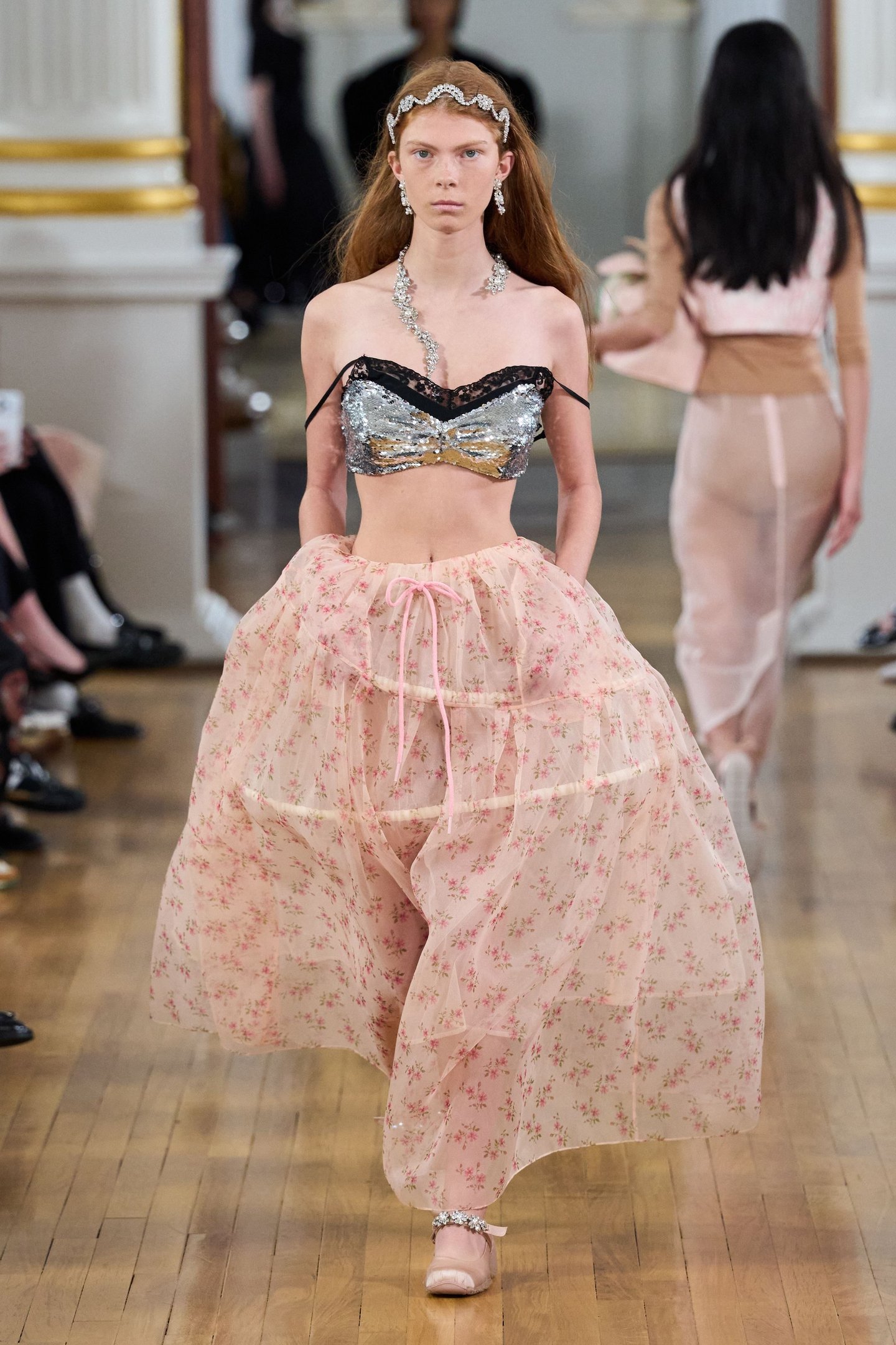 Modelo desfilando com top prateado e saia rosa floral longa na London Fashion Week SS26.
