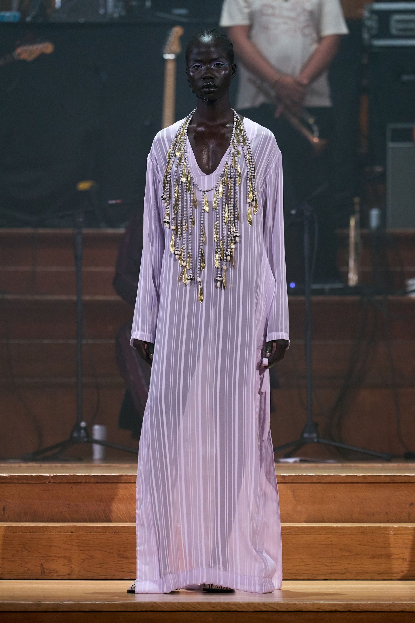 Modelo em desfile com vestido longo listrado lilás e colares intricados, na London Fashion Week SS26.