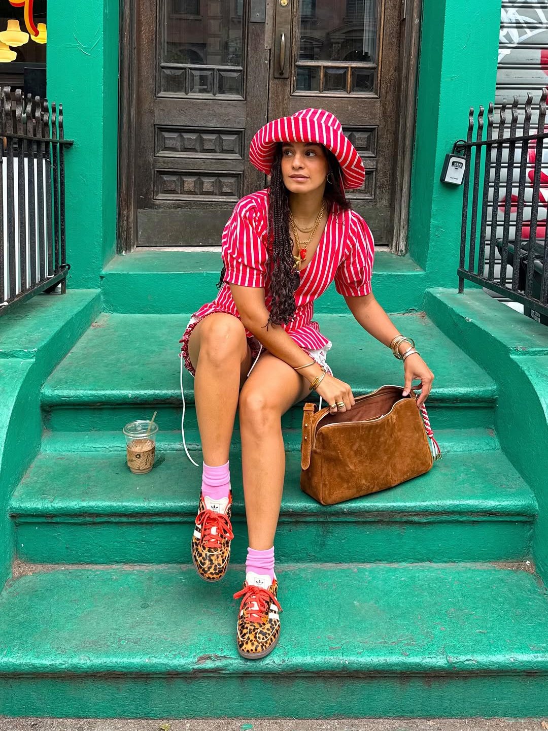 Mulher em vestido listrado vermelho e branco, sentada em escada verde, com bolsa e tênis marrom feminino estampados.