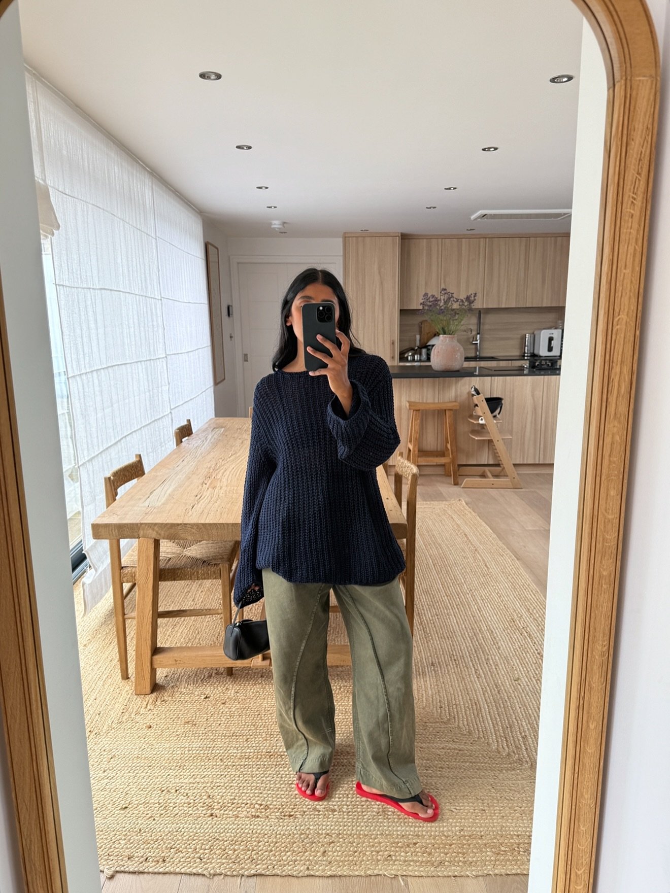 Pessoa com suéter azul, calças verdes e sandálias FiveFingers vermelhas tira selfie em espelho, sala ao fundo.