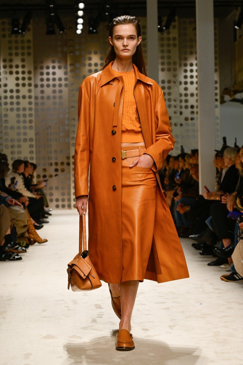 Modelo desfila em look monocromático laranja, com casaco e saia midi, na Milan Fashion Week SS26.