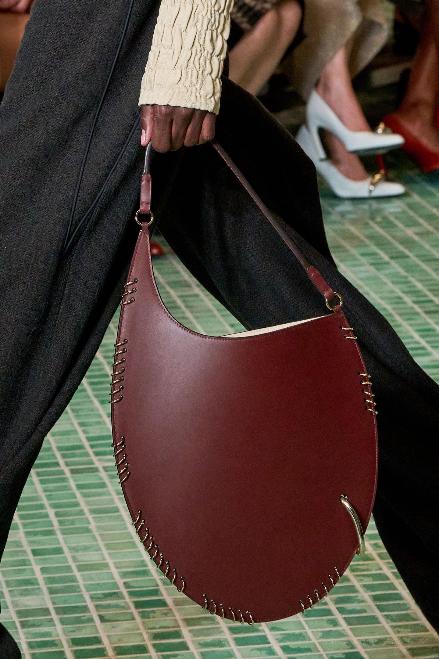 Bolsa marrom com detalhes metálicos, inspirados na moda dos piercings, em desfile de moda.
