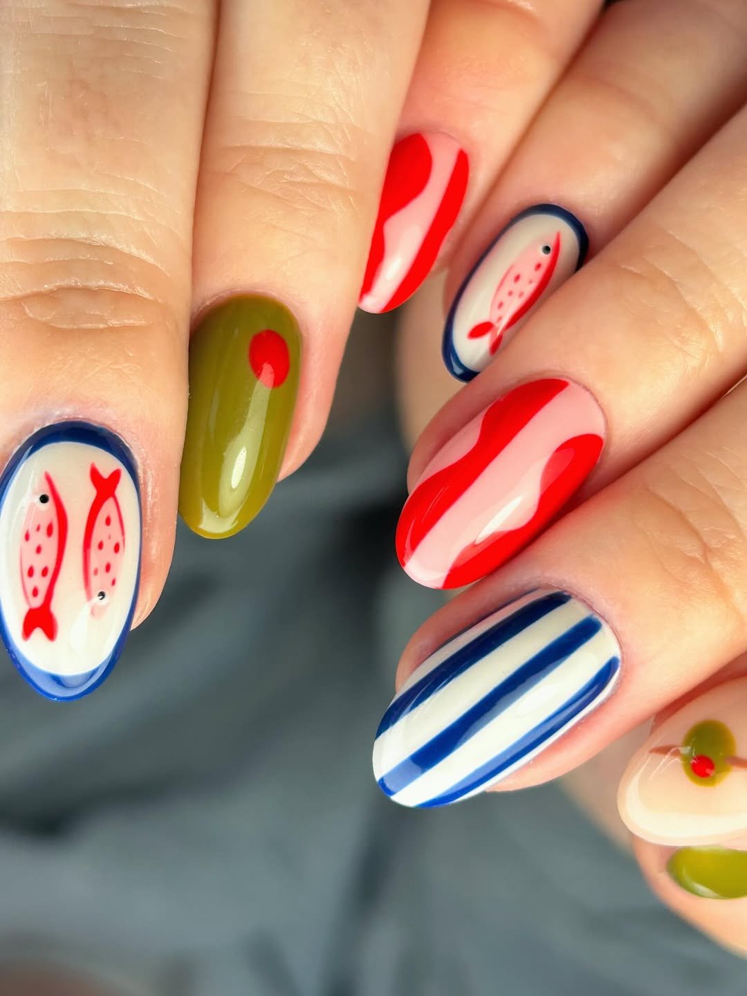 Decoração de unhas de peixes vermelhos, listras azuis e detalhes em verde-oliva, criando um visual colorido e marítimo.