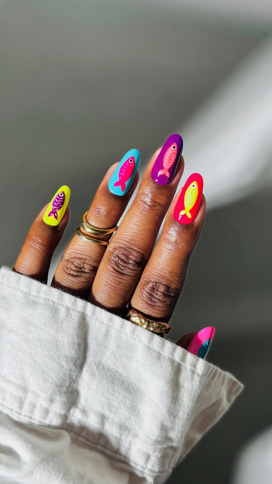Unhas de peixe coloridas com desenhos brilhantes em cada dedo, destacando a arte única.