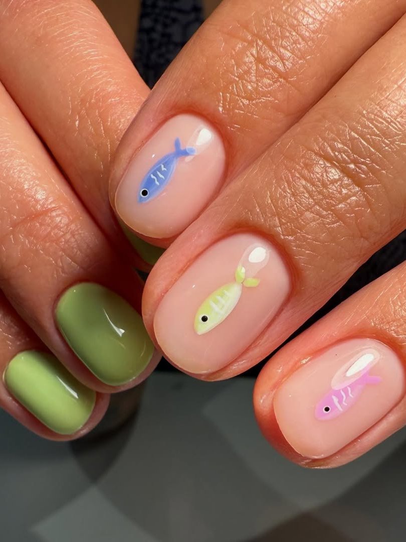 Unhas de peixe coloridos em fundo nude e verde.