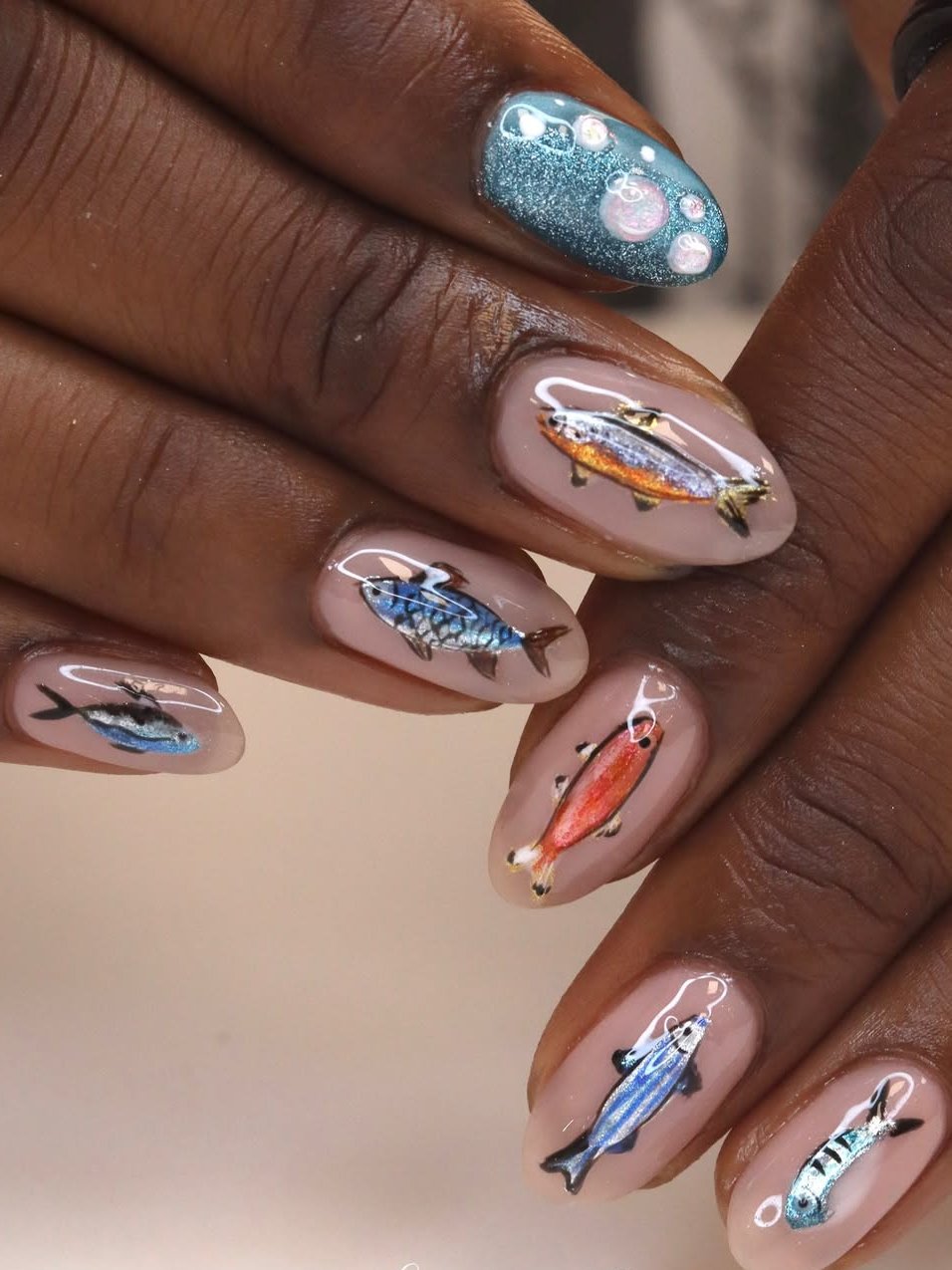 Unhas de peixe coloridos e bolhas sobre esmalte brilhante azul e nude.