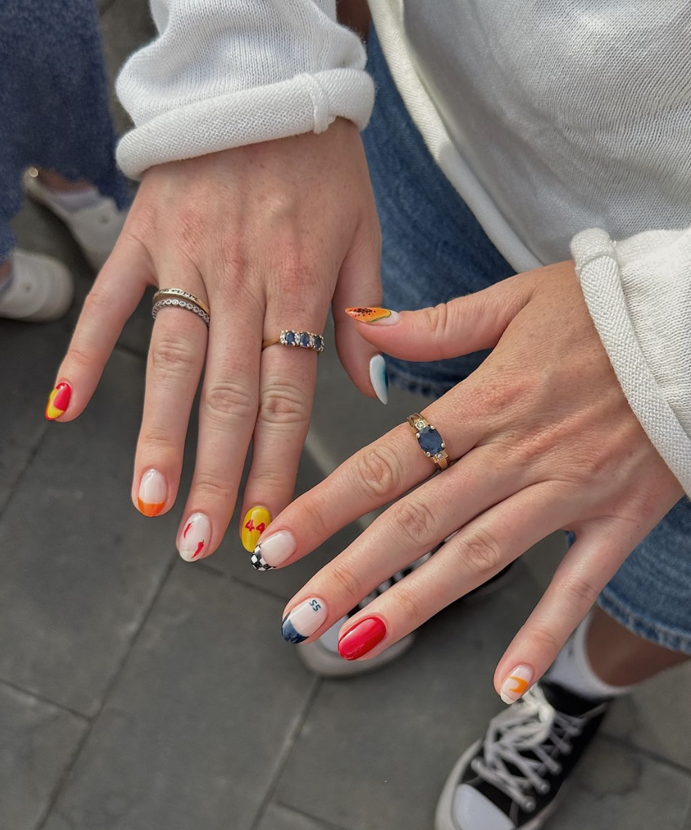 Unhas com nail arts inspiradas na Fórmula 1, exibindo números, padrões xadrez e cores vibrantes.
