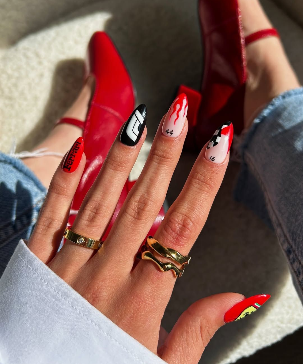 Unhas decoradas com tema nail arts de Fórmula 1; detalhes vermelhos, pretos e brancos, referências a marcas e números.