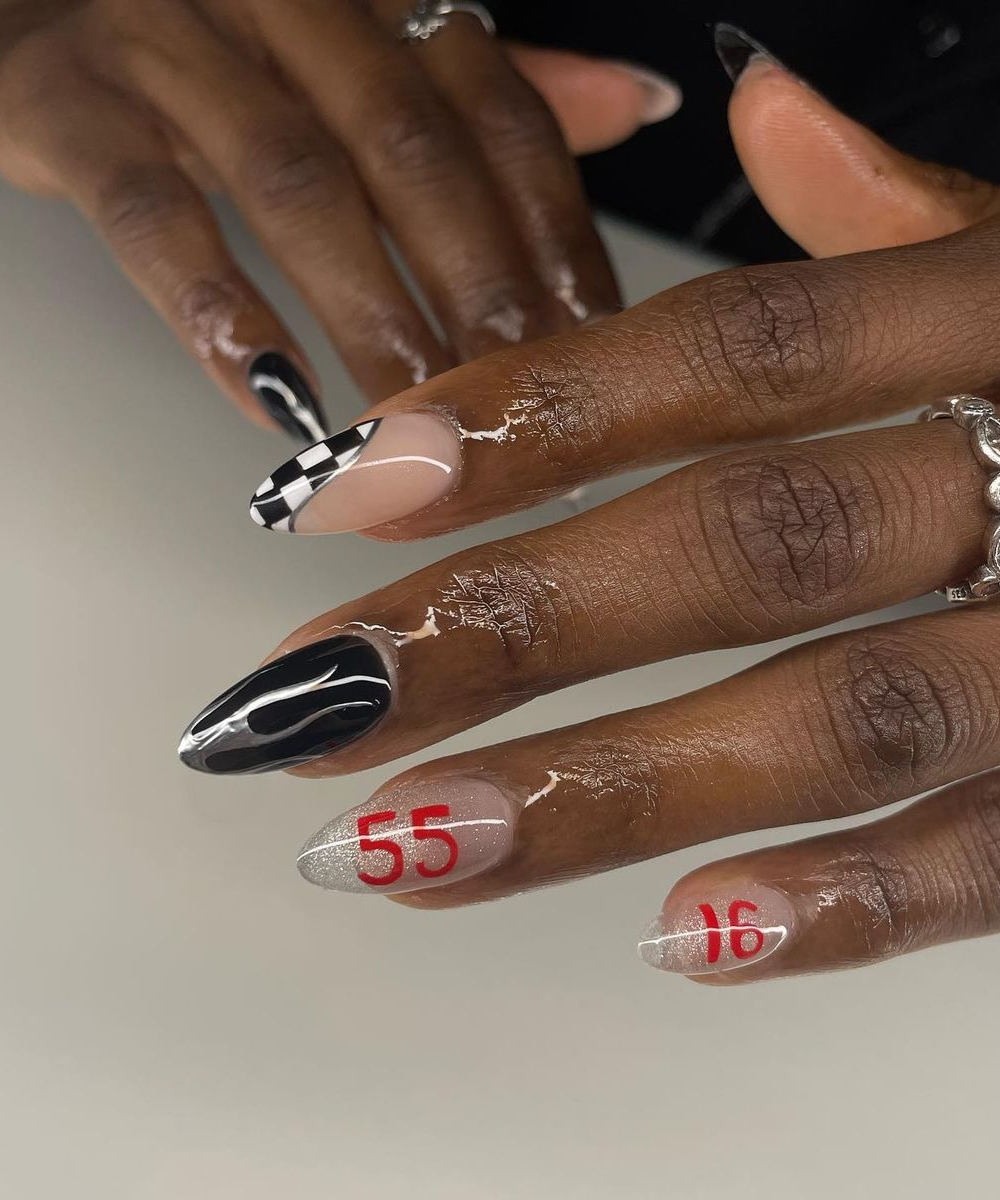 Unhas decoradas com tema de Fórmula 1, incluindo padrão quadriculado e números 55 e 16 em vermelho.