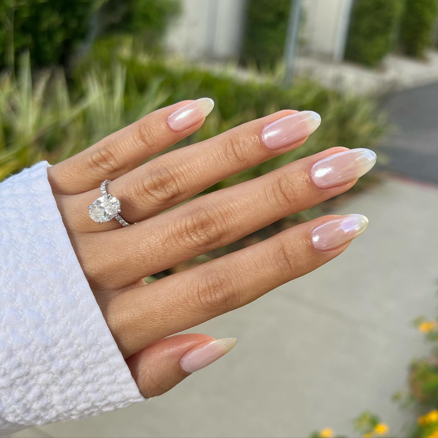 Unhas com esmalte perolado, estilo primavera, com anel de diamante no dedo anelar.