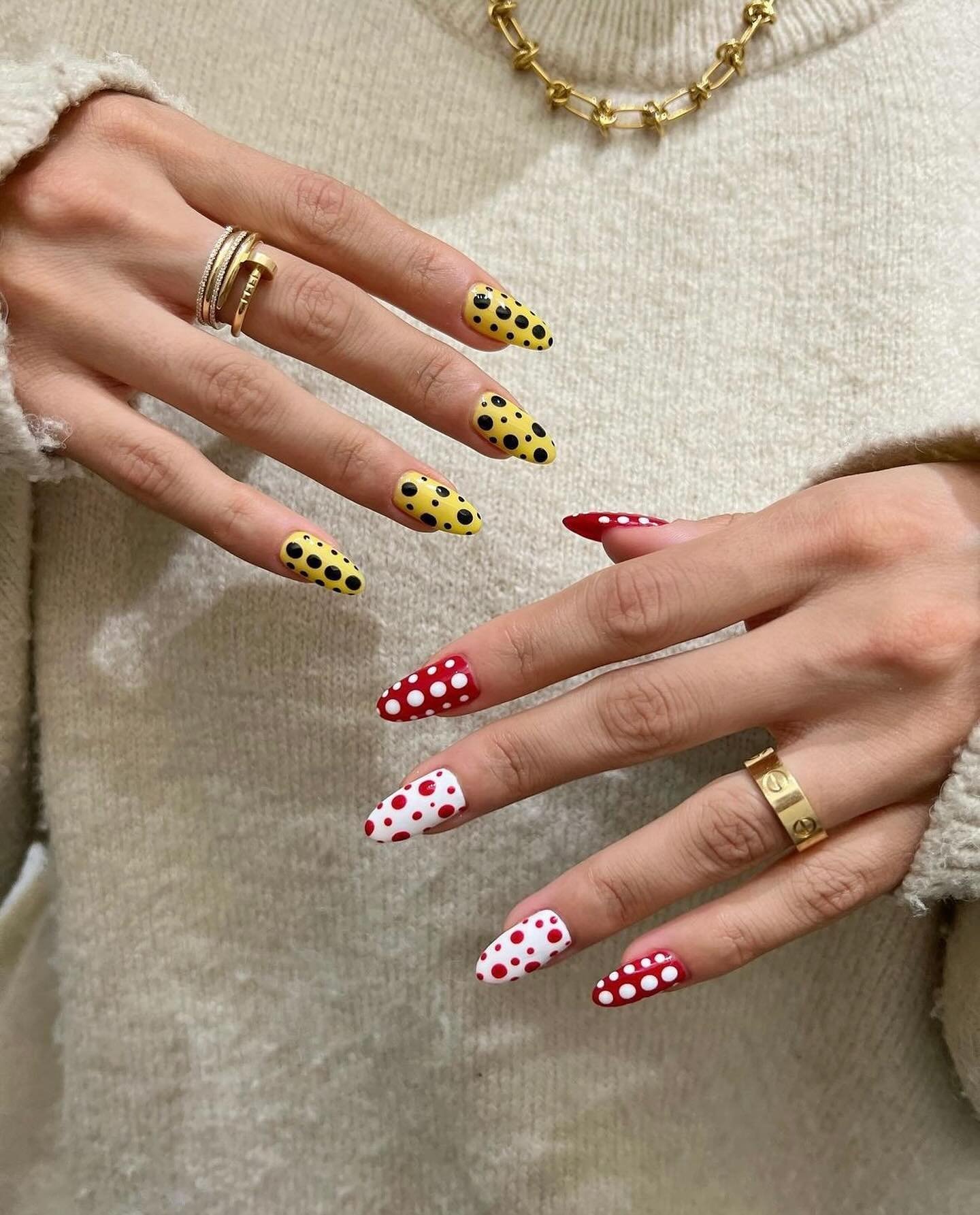 Unhas decoradas com estampas de bolinhas: amarela e preta na mão esquerda, vermelha e branca na direita, estilo primavera.