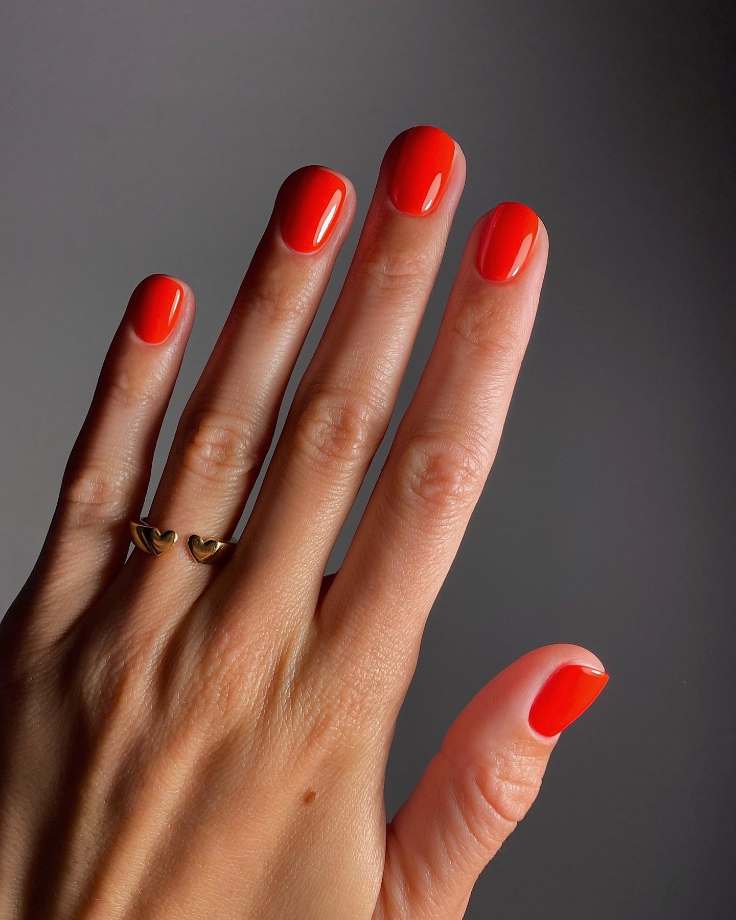 Unhas para primavera curtas pintadas de vermelho com anel dourado de corações. Estilo elegante para primavera.
