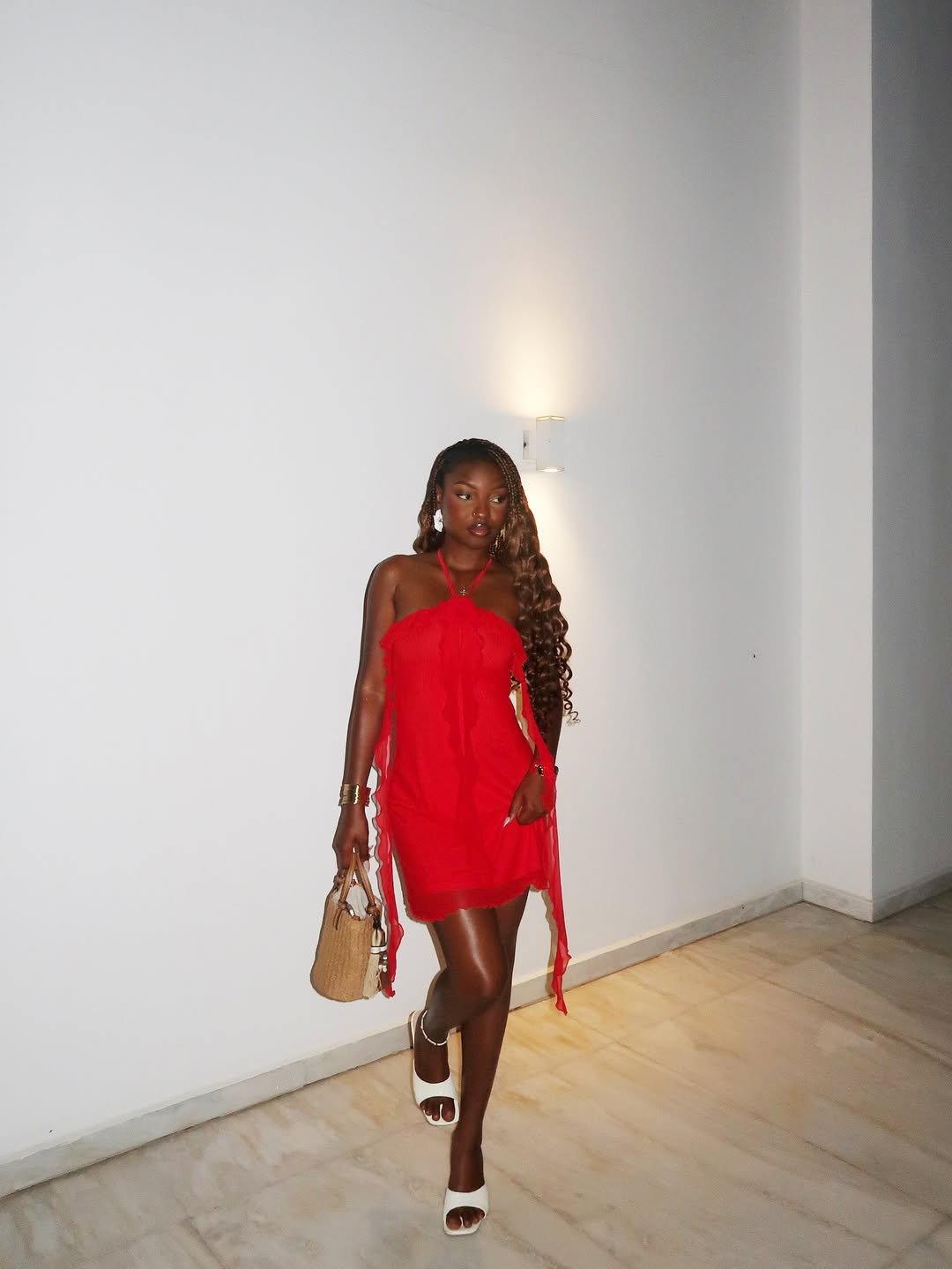 Pessoa caminhando em corredor de mármore, vestindo vestido vermelho tomate, segurando bolsa de mão.