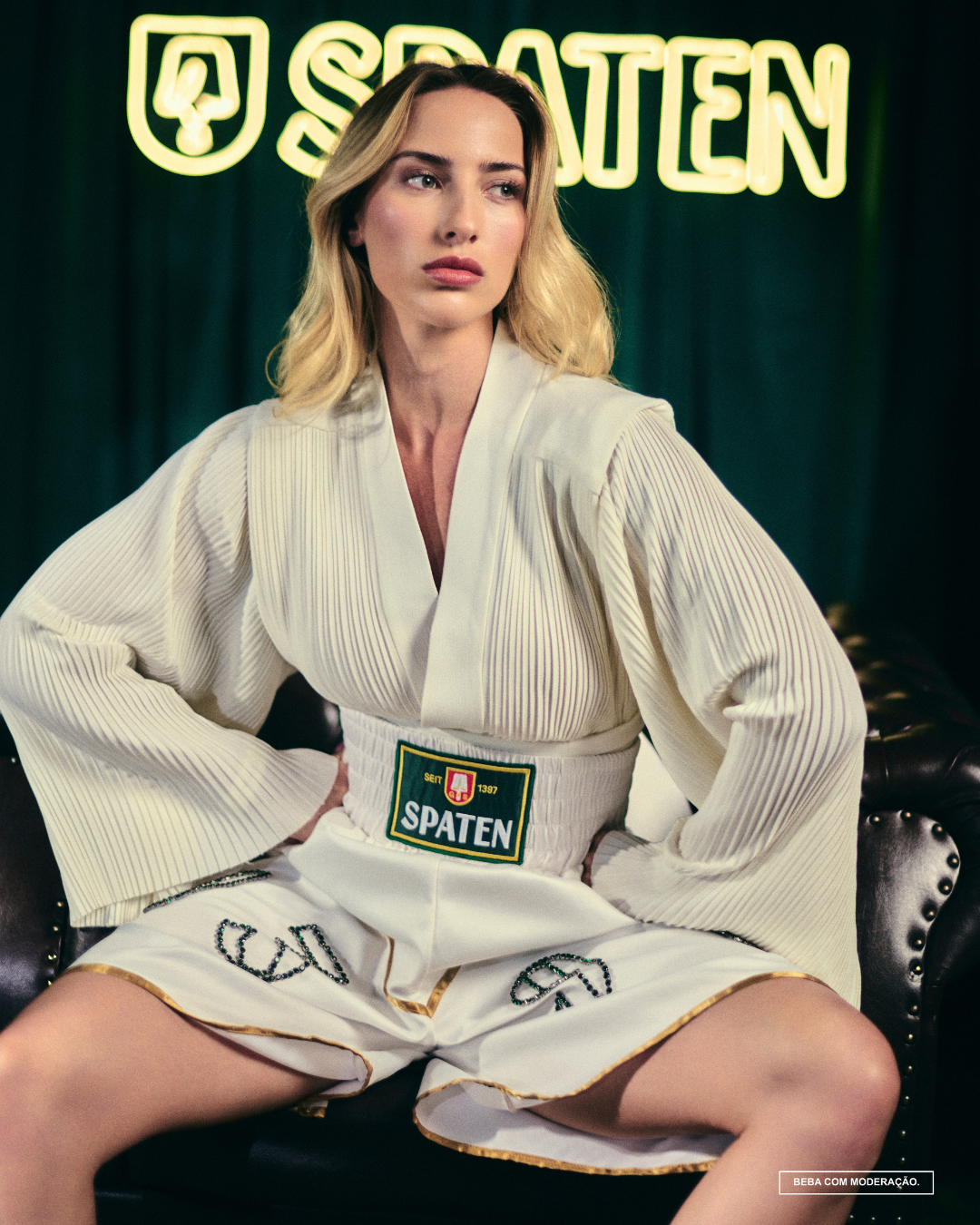 Pessoa sentada em poltrona, vestindo roupão branco de boxe com a marca Spaten em cinto, diante de painel iluminado.o que é upcycling
