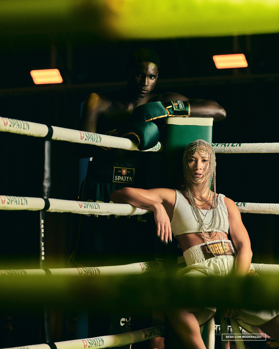 Dois indivíduos em um ringue de boxe, um usando luvas verdes e outro com roupa adornada, sob luzes amarelas. o que é upcycling