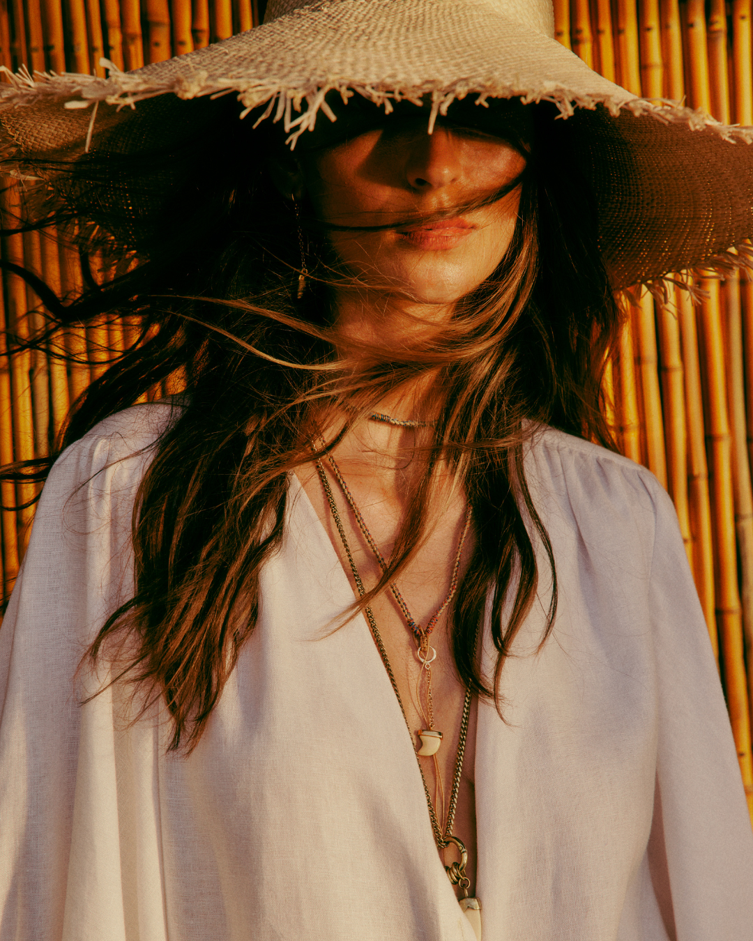 Mulher usando chapéu de palha largo e blusa leve, destacando tendências de alto verão.