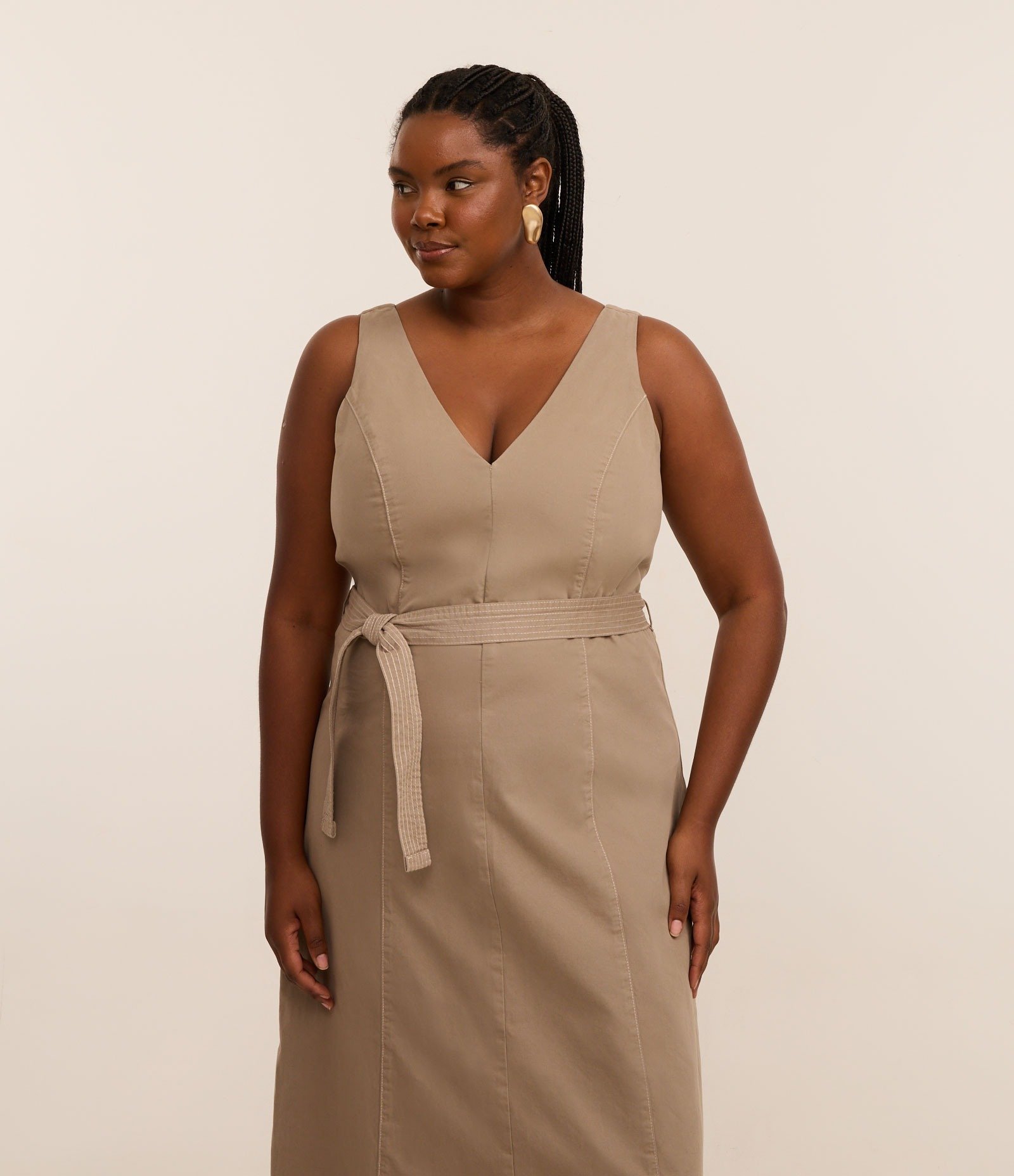 Vestido em tom neutro, confeccionado em algodão regenerativo, destaca-se pela modelagem que valoriza a silhueta. O decote em V e a cintura marcada com faixa proporcionam elegância. A combinação traz conforto e  algodão regenerativo