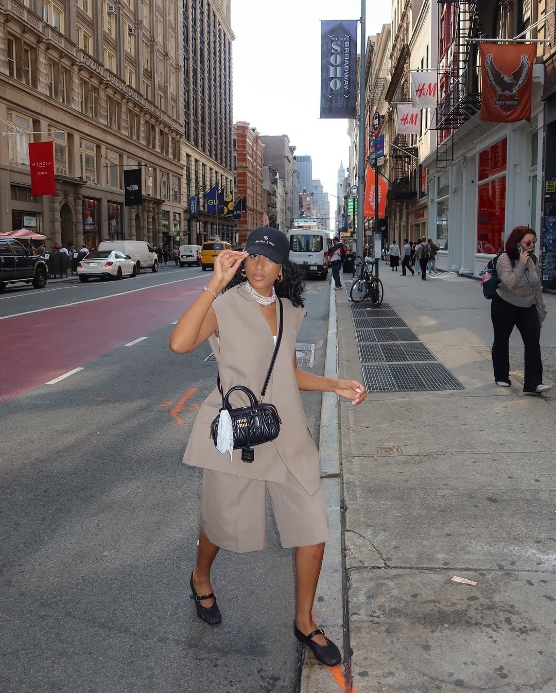 A imagem apresenta uma mulher estilosa usando um looks com bermuda em um ambiente urbano. Ela veste um conjunto em tom neutro, que combina uma blusa sem mangas e bermuda, criando uma silhueta elegante.