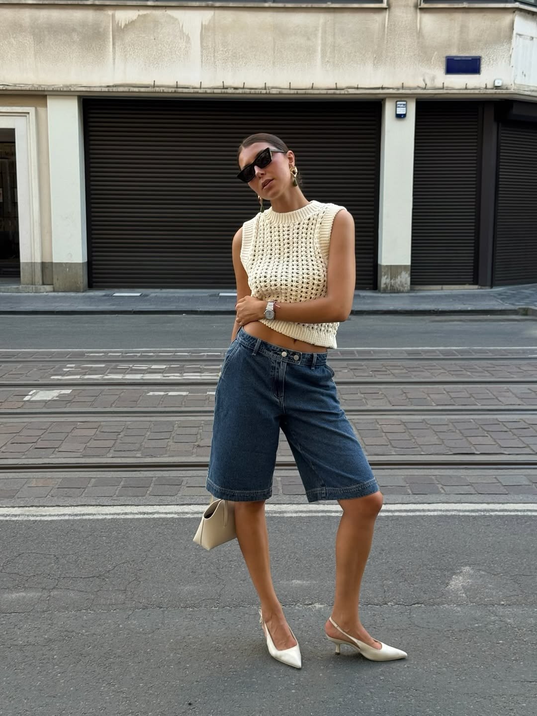 O looks com bermuda apresenta uma combinação estilosa e moderna. A modelo usa uma blusa de tricô creme, que traz textura, e bermuda jeans, criando um contraste interessante.