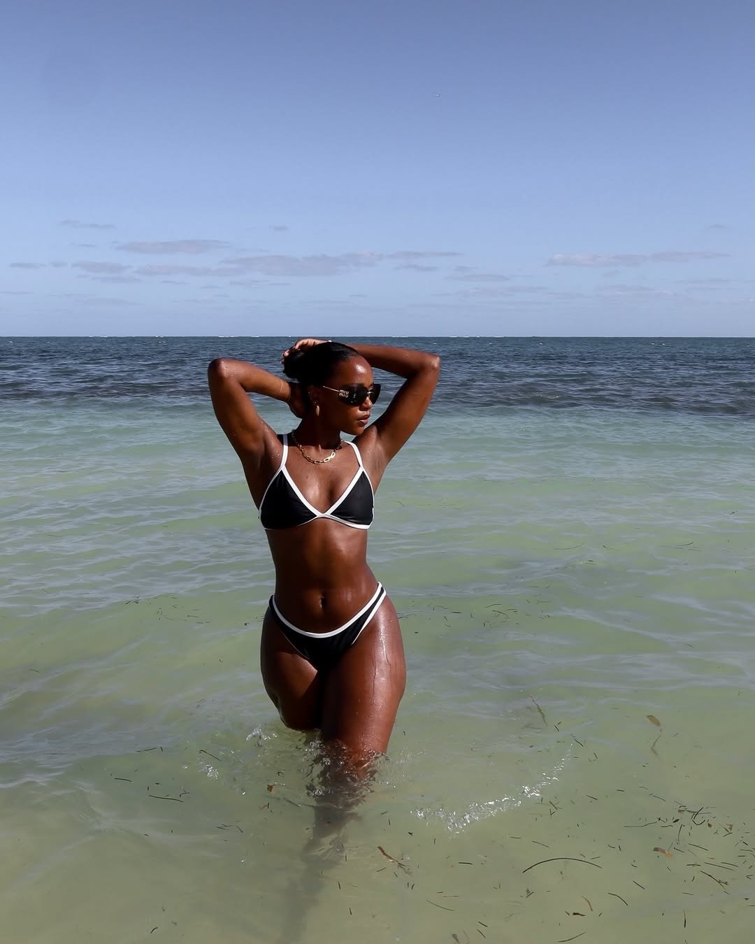 Modelo usa um biquíni simples, com design de triângulo nas cores preto e branco, enquanto está na água. O look destaca-se pela elegância minimalista e conforto, ideal para momentos de lazer à beira-mar.