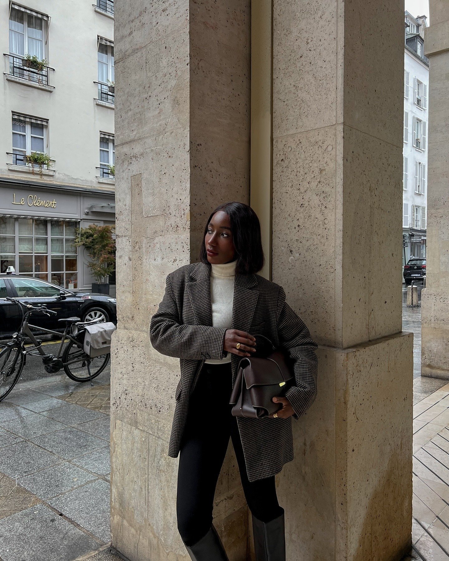 A blusa canelada básica de gola alta, em tom neutro, se destaca sob um blazer xadrez oversized, criando um visual elegante e moderno. A combinação com calças pretas justas e botas de cano alto complementa o look, ideal para dias frios.