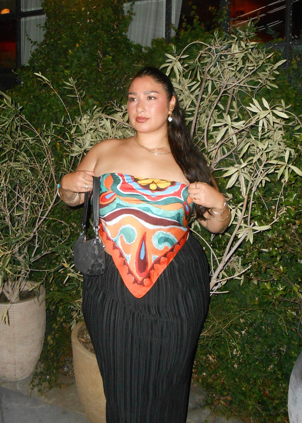 A blusa de cetim feminina, com design vibrante e estampas coloridas, destaca-se na composição do look. A peça, de modelagem ajustada, valoriza a silhueta, enquanto a saia plissada complementa o visual com elegância.