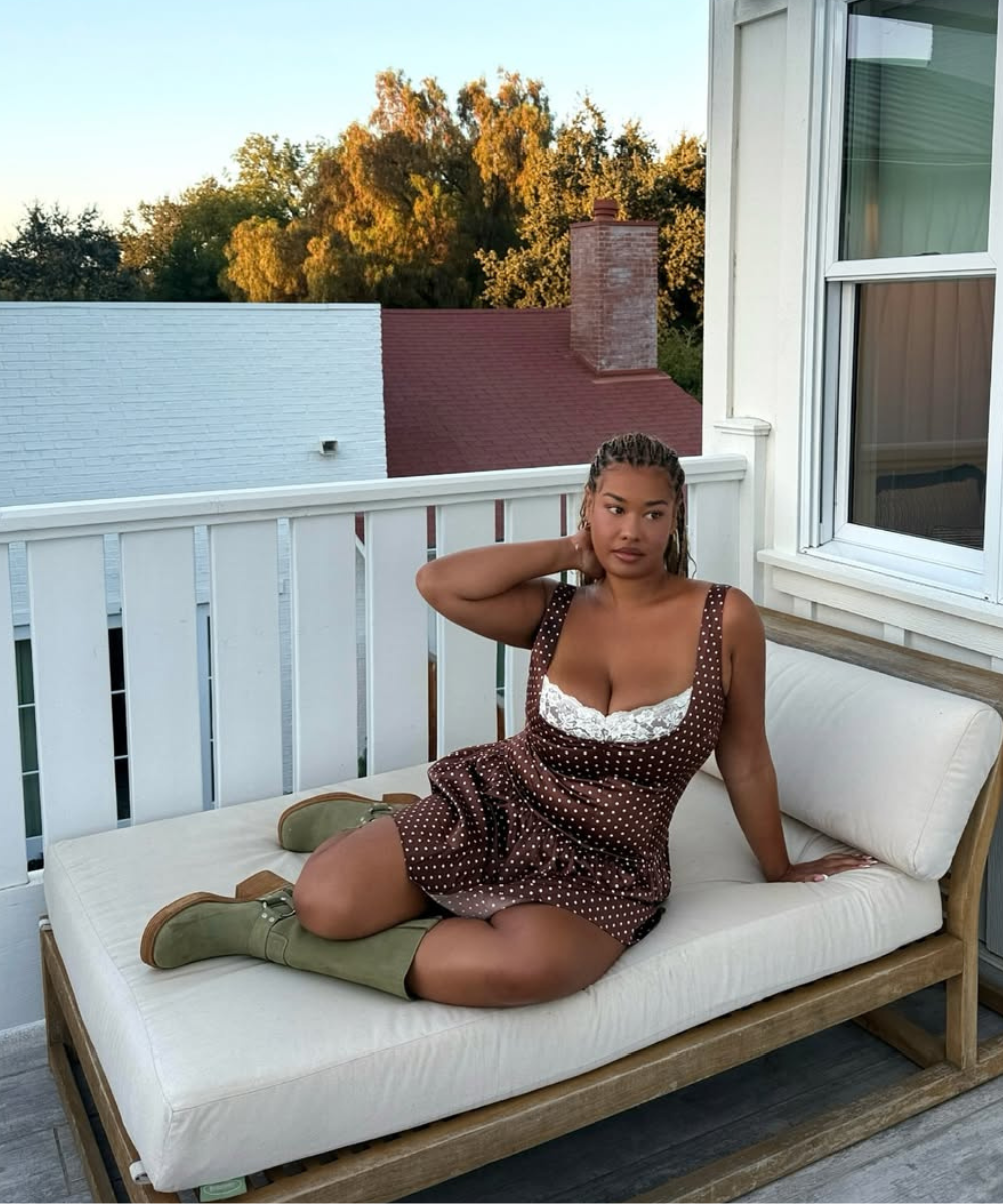 Mulher sentada em uma chaise no terraço, usando botas verdes, calçado tendência, e vestido de bolinhas.