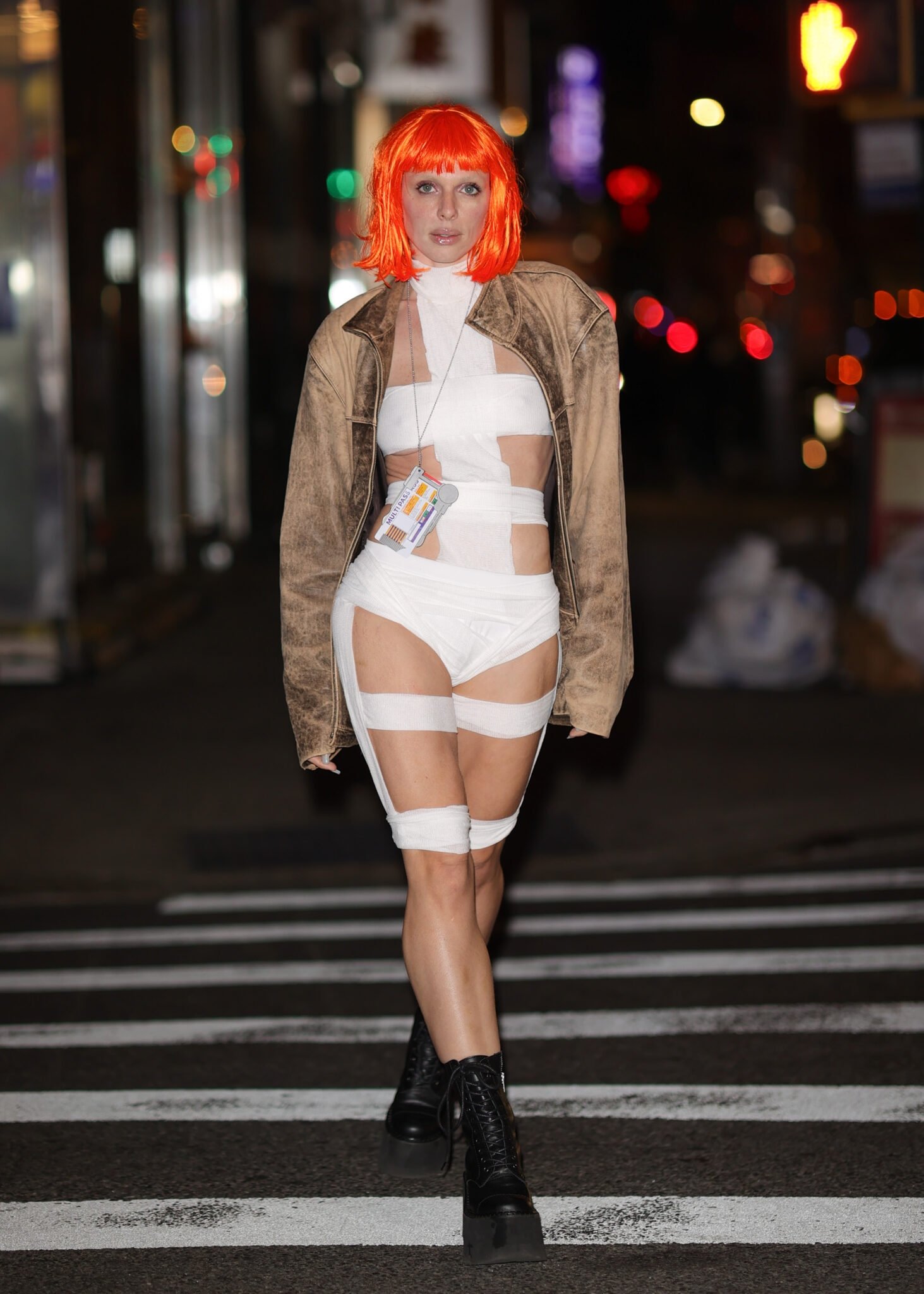 Mulher usando fantasia de Halloween feita de faixas brancas e peruca laranja, desfilando à noite na rua.