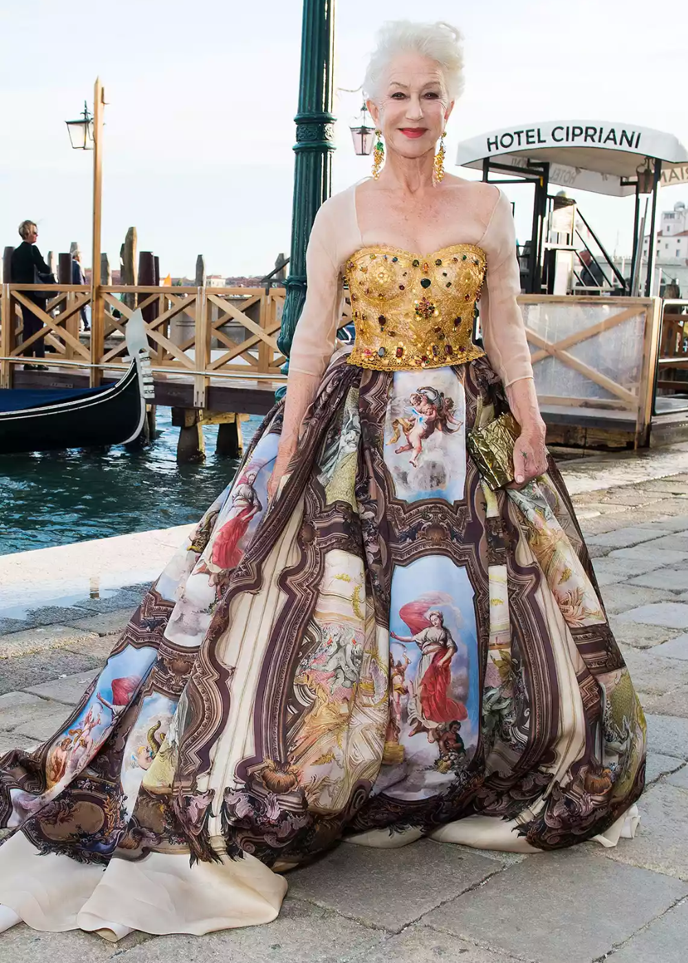 Mulher em vestido estampado luxuoso com corselete dourado, próxima a um canal em Veneza.