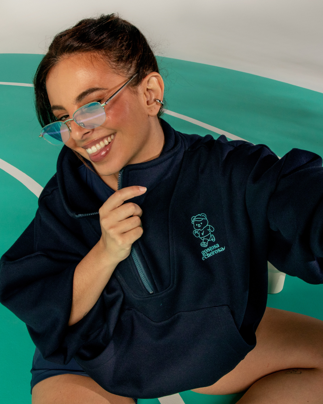 Pessoa sorridente de óculos e jaqueta azul em fundo verde. collab Lela Brandão e Rexona Desodorante corporal.