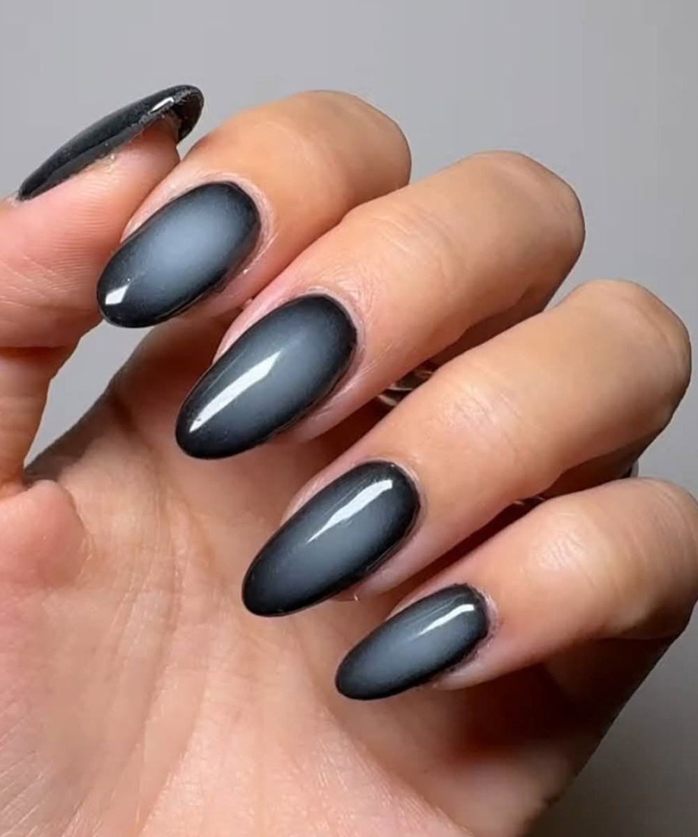 As unhas estão pintadas com um esmalte descasque em tons de preto e cinza, apresentando um efeito ombré elegante.