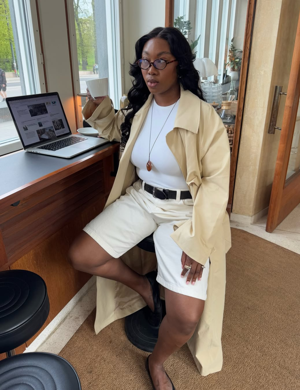 A bermuda feminina branca apresenta um corte moderno e casual, combinando perfeitamente com uma blusa branca e um trench coat bege, criando um visual sofisticado e elegante.